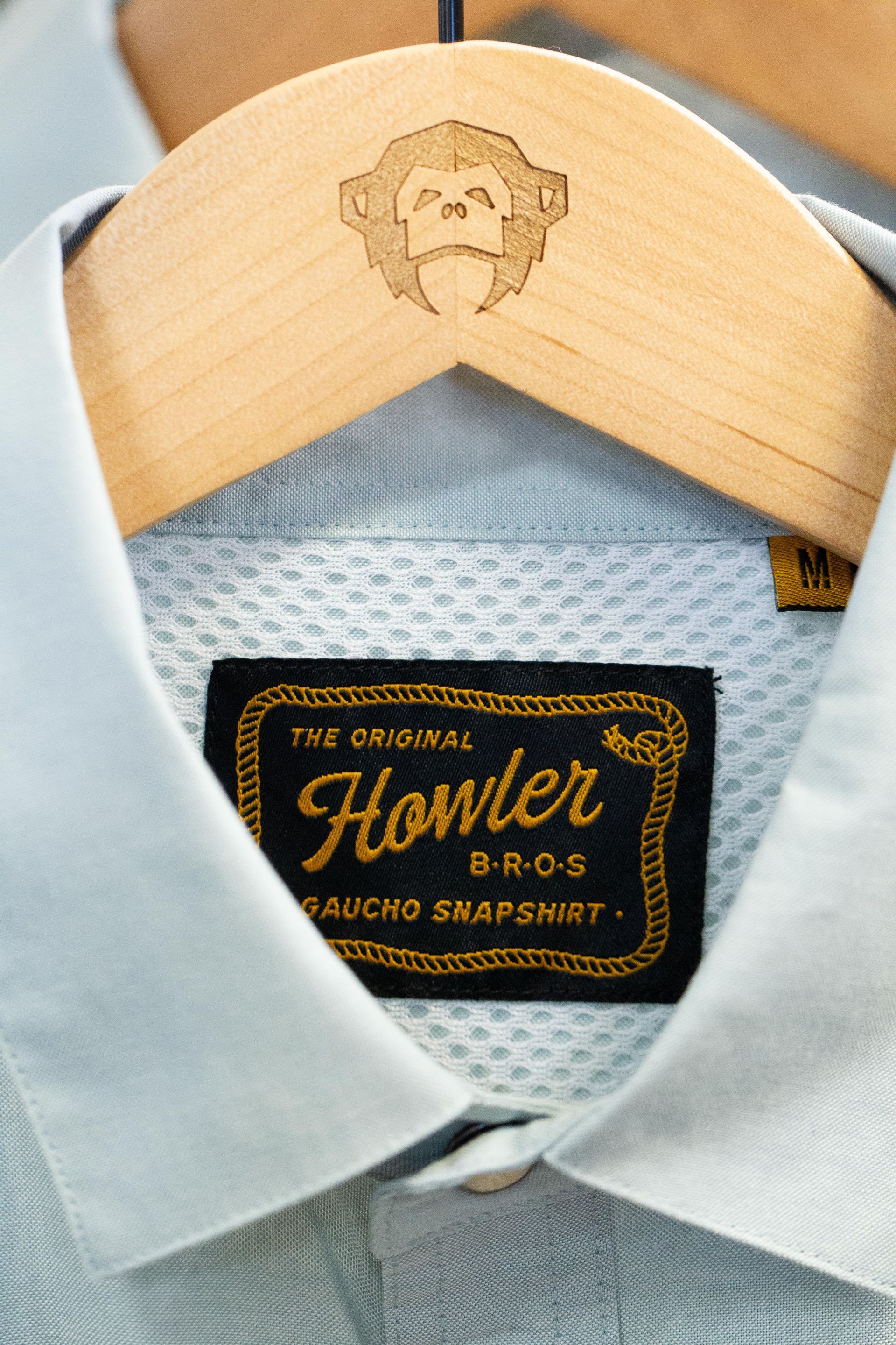 A light blue polo shirt on a wooden hanger, with a monkey logo and a 