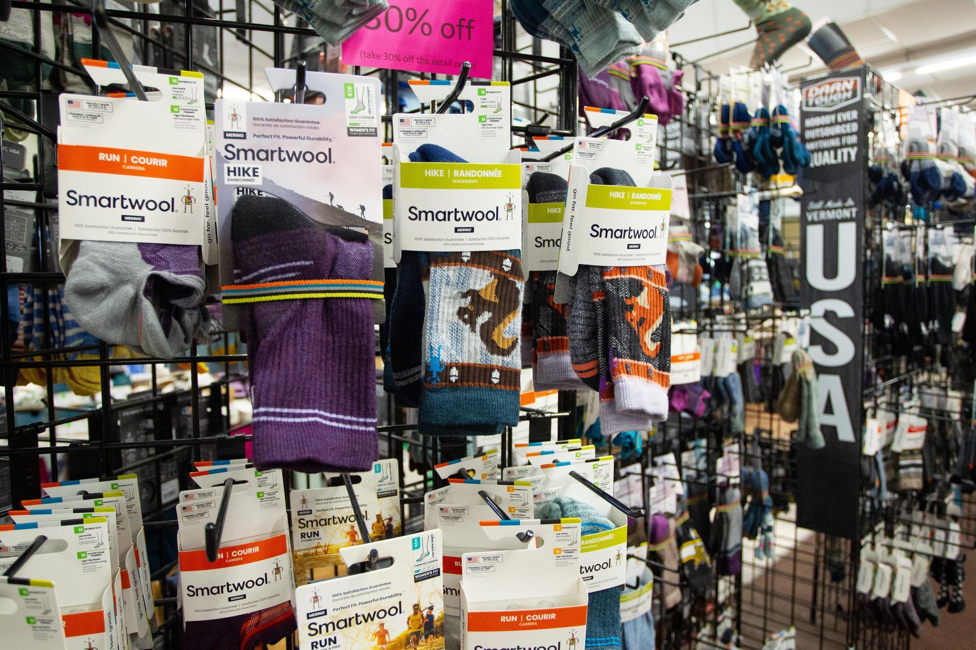 Display of Smartwool socks in a store. Many pairs in various colors and patterns hang on a grid rack, with a 