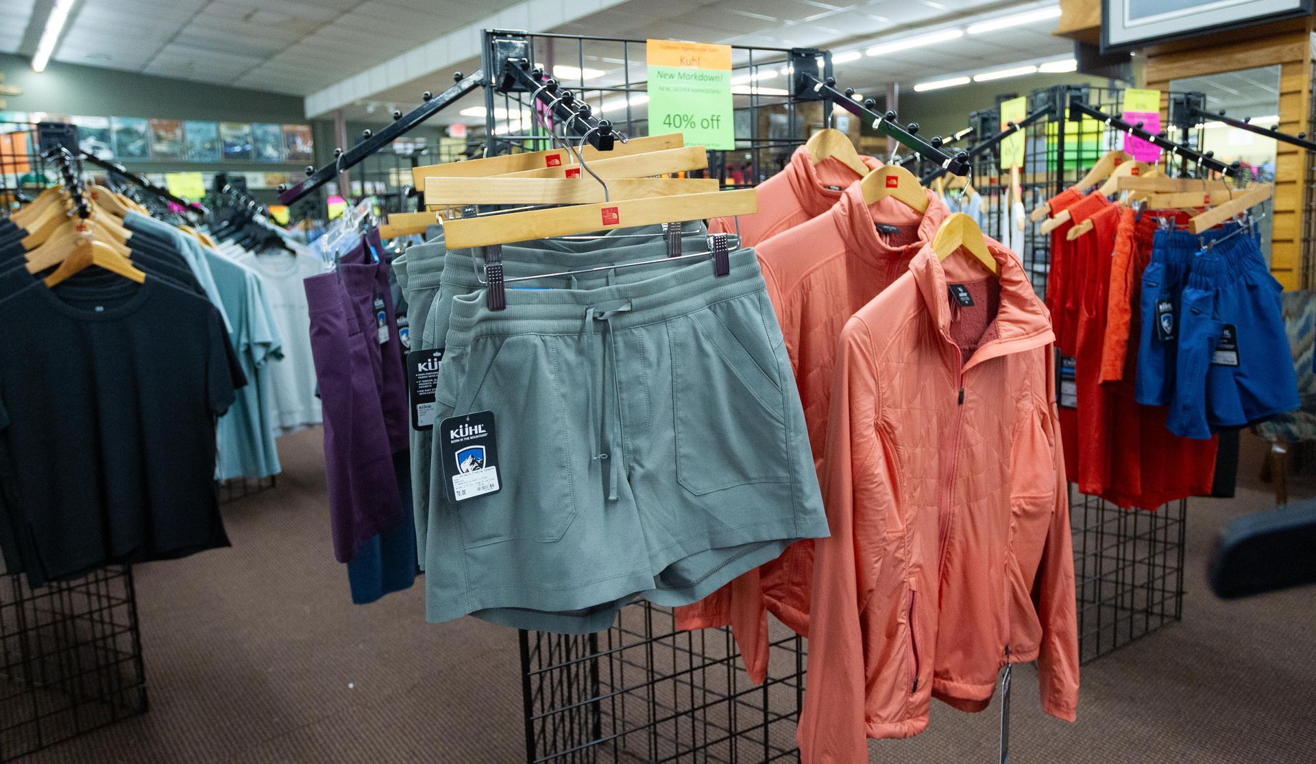 Clothing racks in a store display various items, including shorts, jackets, and shirts in a range of colors like black, blue, and orange.