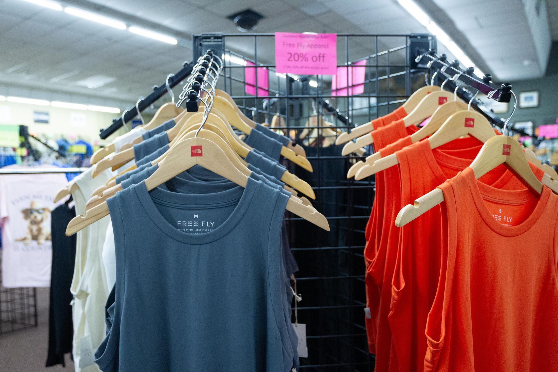 Clothing rack in a store displaying sleeveless shirts in various colors, including orange and gray, with a 