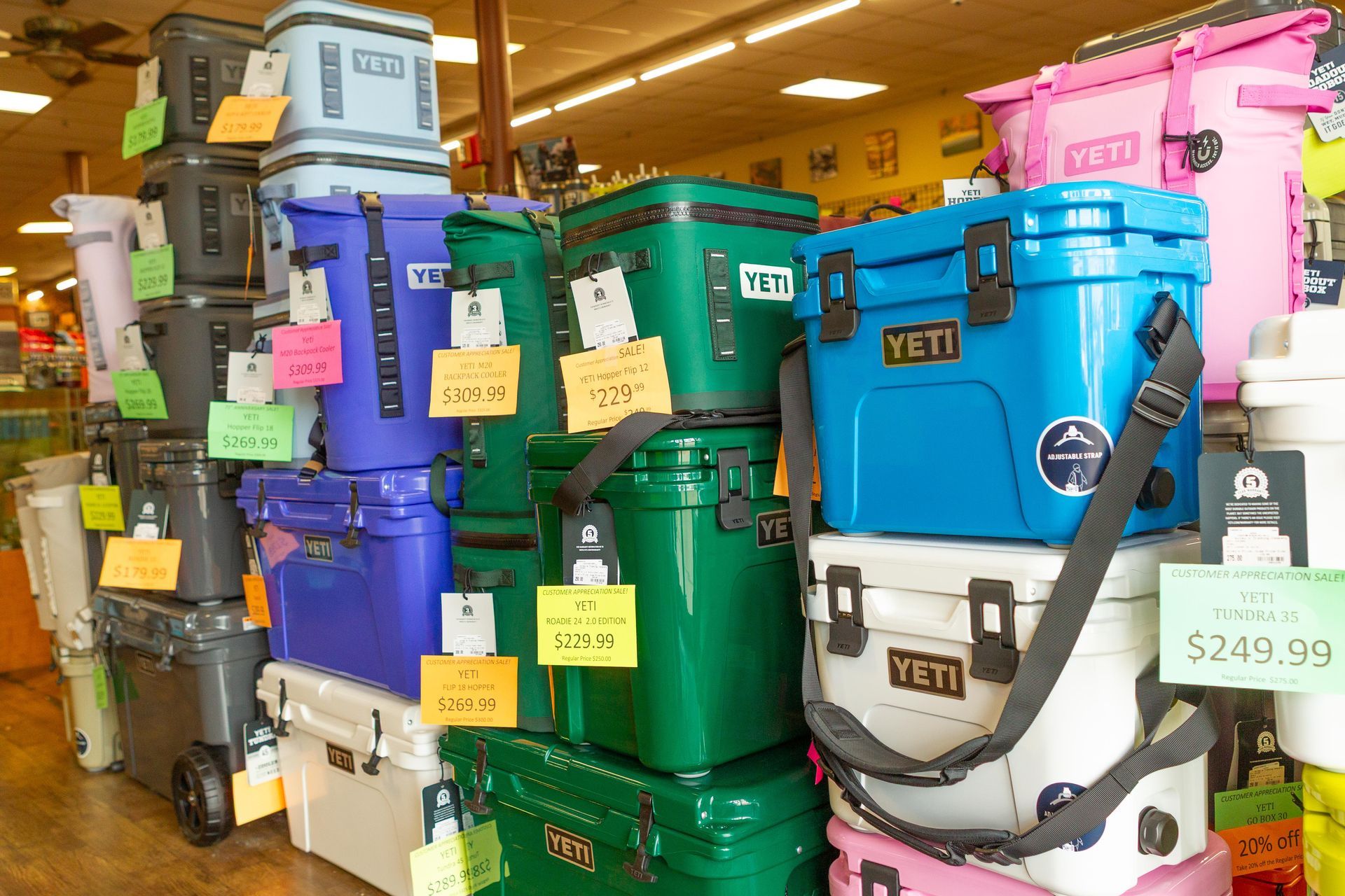 Coolers of various colors, mostly Yeti brand, stacked for display in a store. Price tags are attached to some.