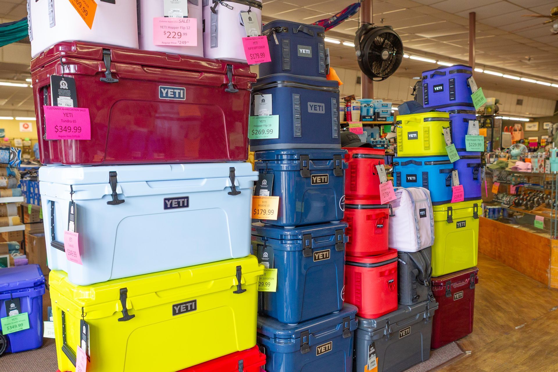 Stacked display of colorful Yeti coolers inside a store. Various sizes and hues like red, blue, and yellow are shown.