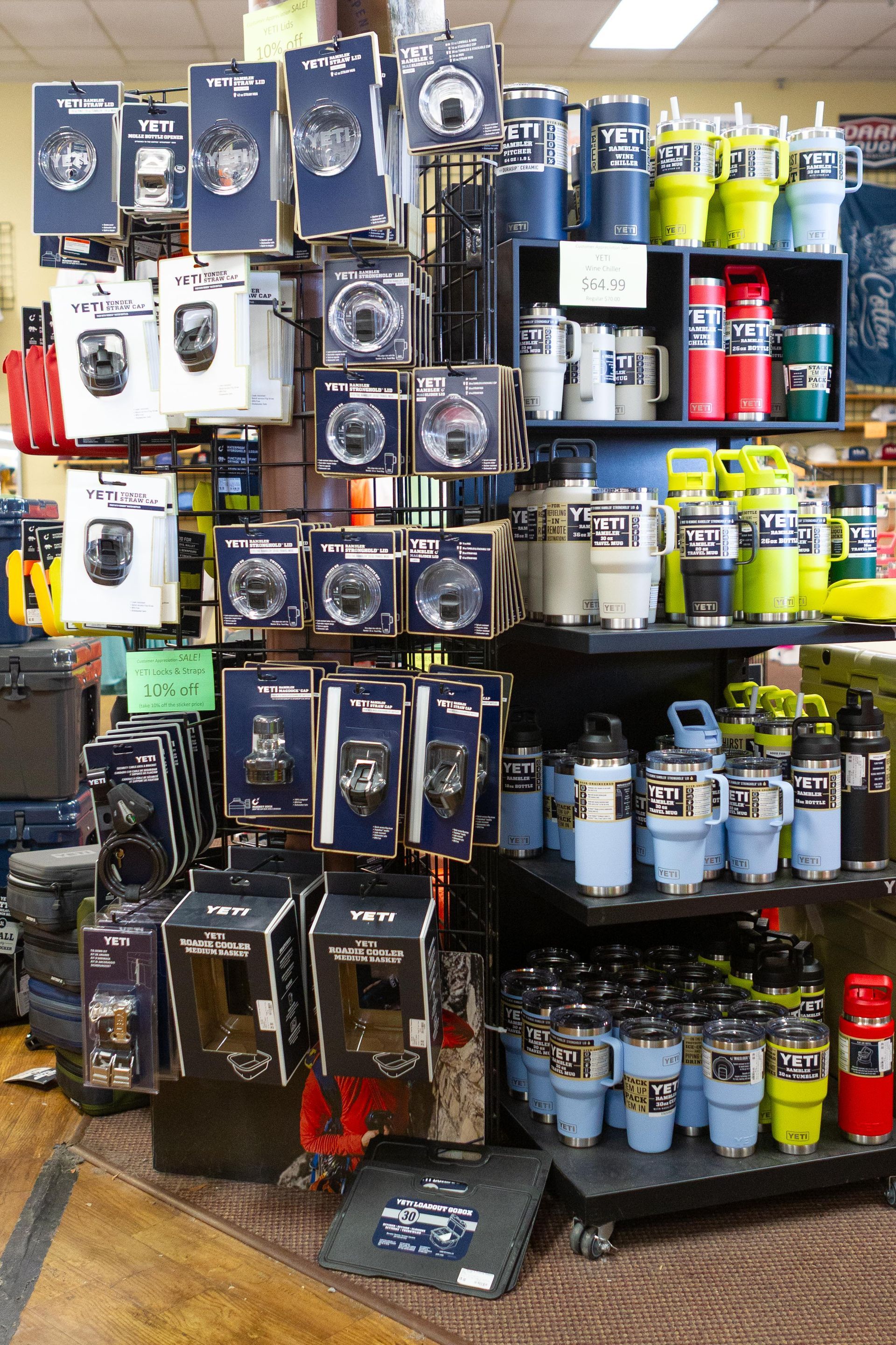Display of drinkware, coolers, and accessories in a store. Products in various colors like blue, white, red, and yellow are arranged on shelves and a stand.