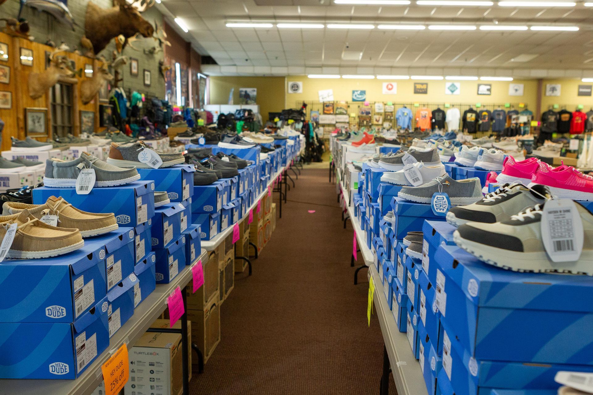 Inside a shoe store, rows of shoes on blue boxes line the aisles. Taxidermied animal heads hang on the wall.