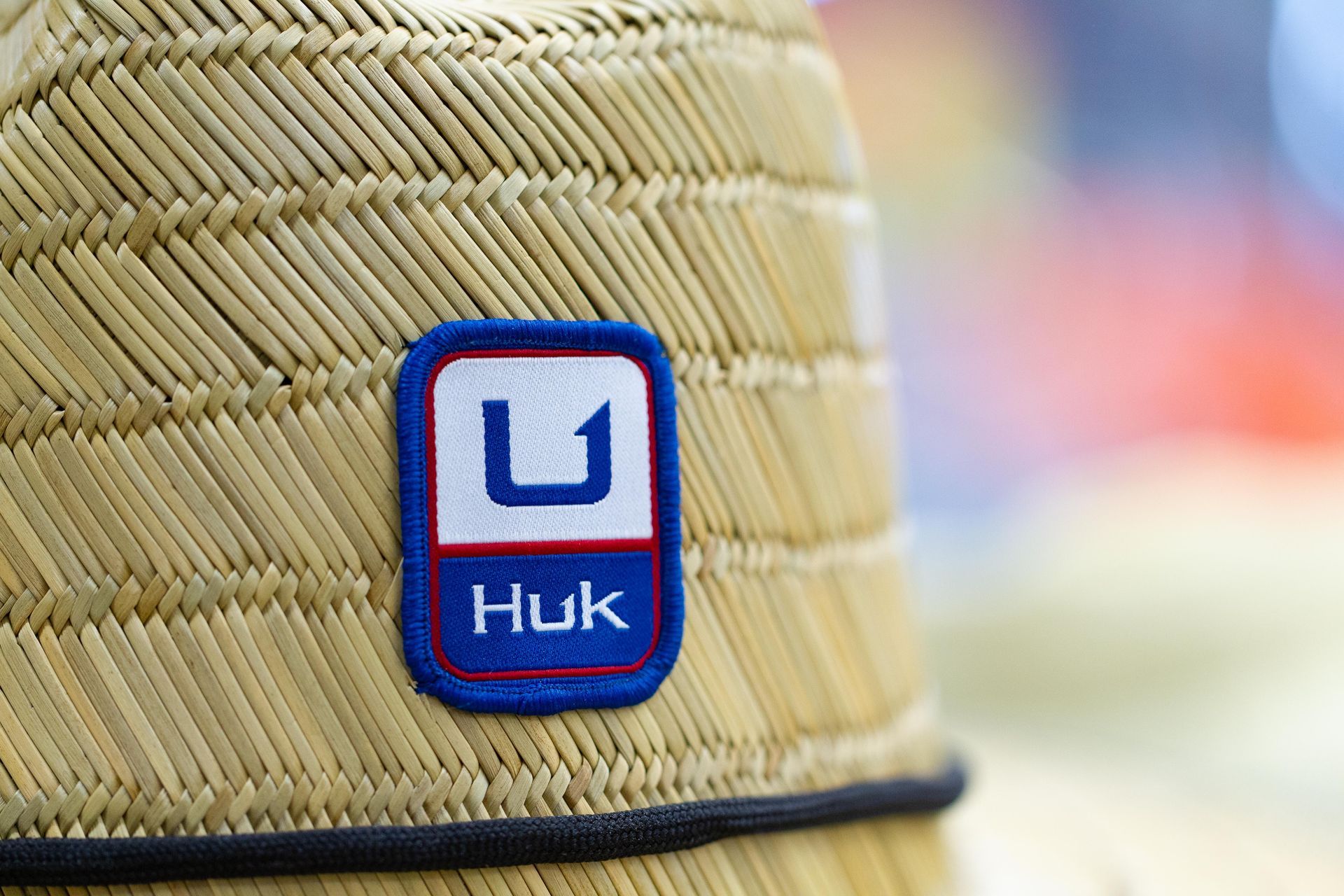 Close-up of a woven straw hat with a blue and white Huk logo patch.