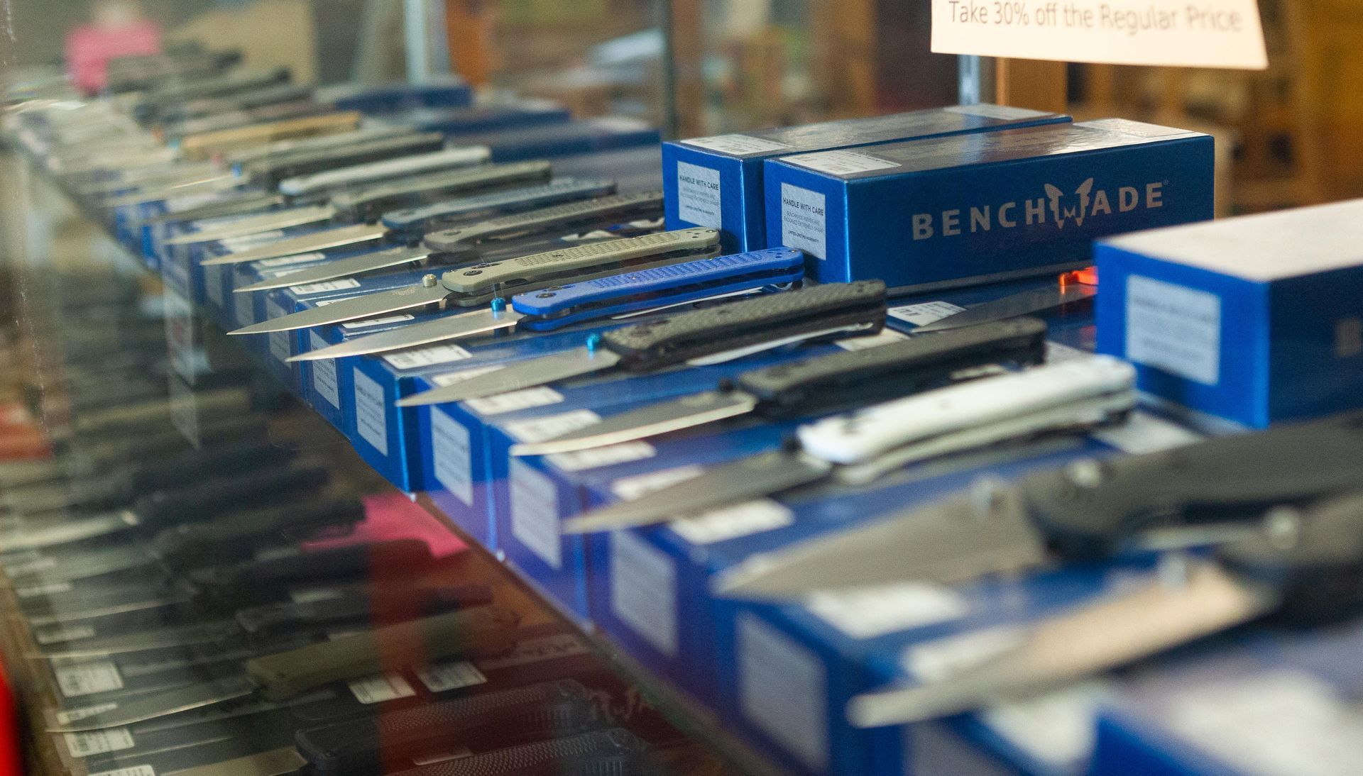 A display case filled with open and closed knives, including several in blue boxes marked