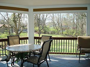 A screened in porch with a table and chairs and a view of trees.