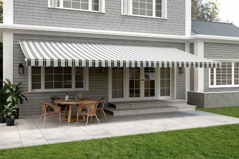 A house with a striped awning over a patio with a table and chairs.