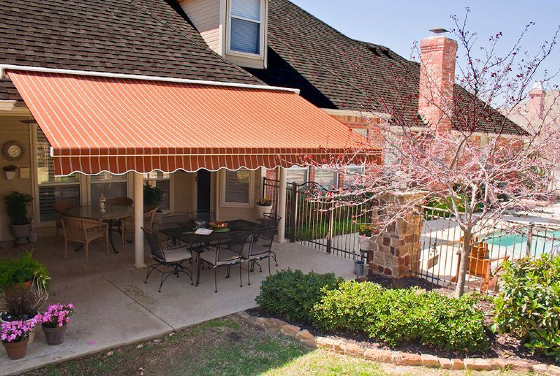 A patio with a table and chairs under an awning next to a pool.