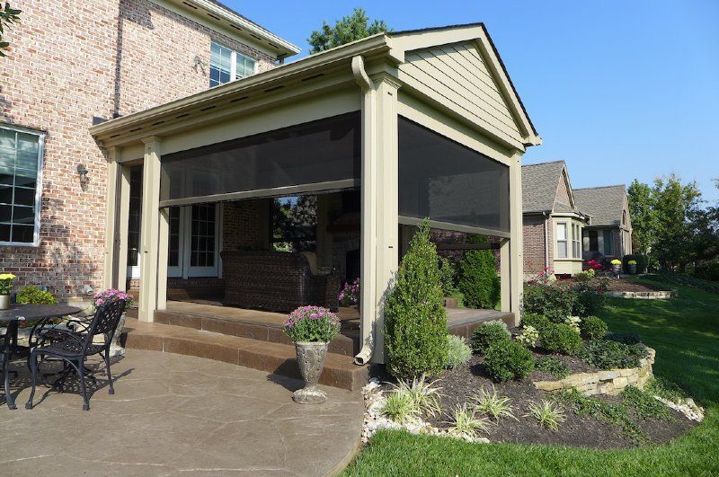 A screened in porch with a table and chairs in front of a brick house.