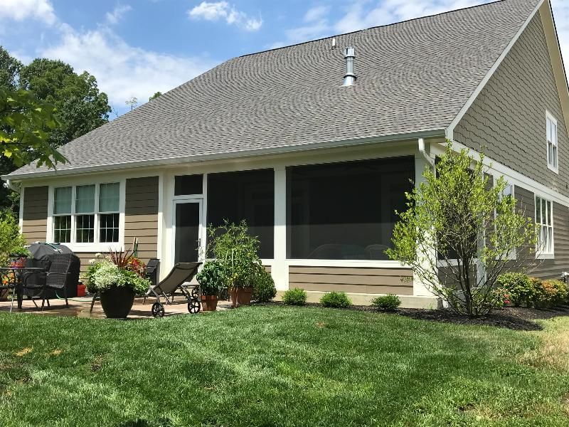 A house with a screened in porch and a large lawn in front of it.