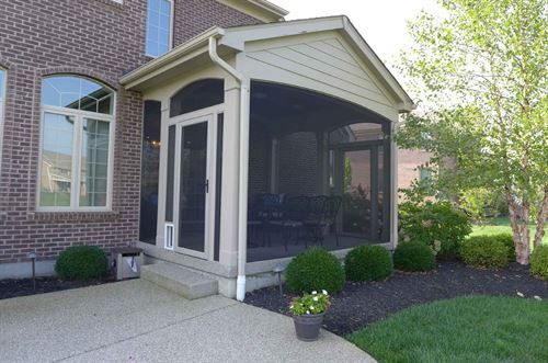 A screened in porch with a brick house in the background.