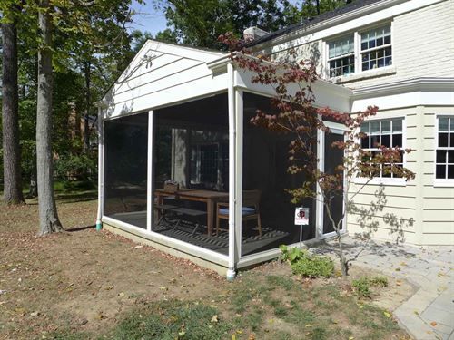 A screened in porch with a table and chairs in front of a house.
