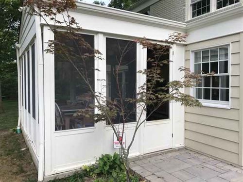 A screened in porch next to a house with a tree in front of it.