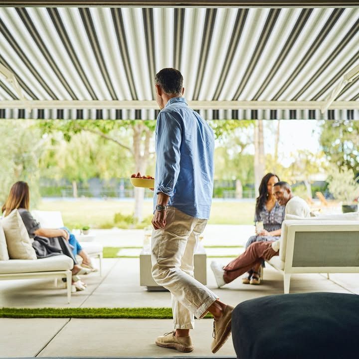 A man is walking towards a group of people sitting on a patio under an awning.