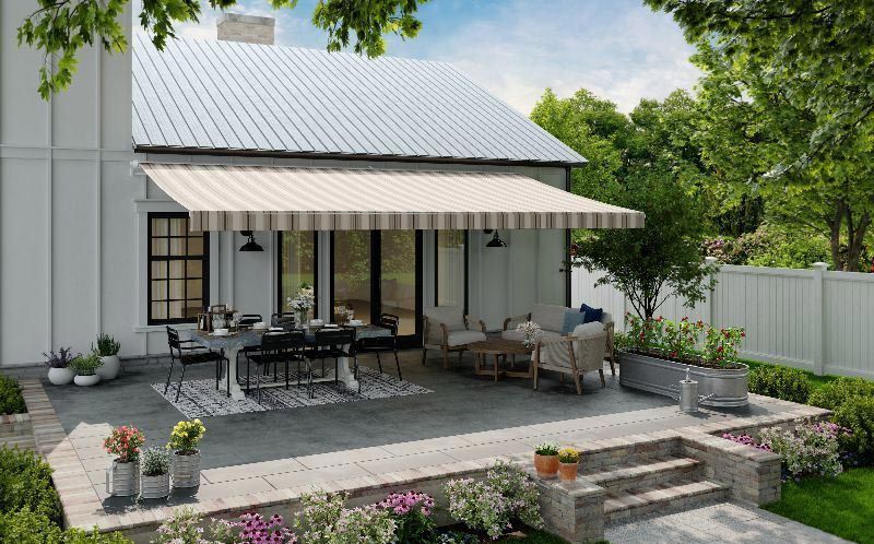 A white house with a patio with a striped awning over it.