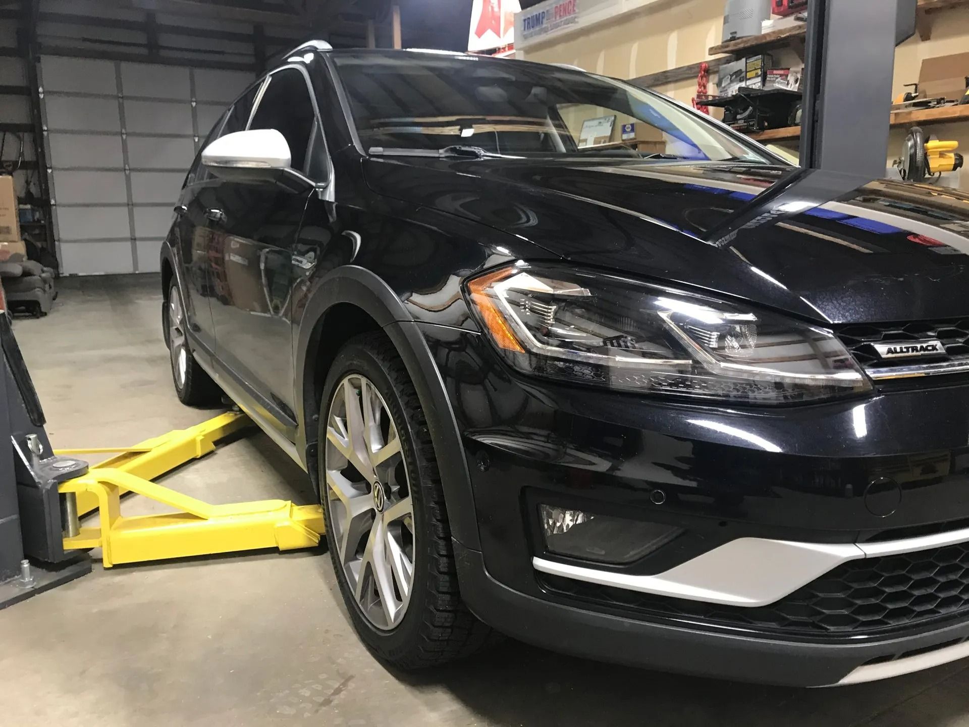 Black Volkswagen Golf Alltrack on a yellow car lift in a garage.