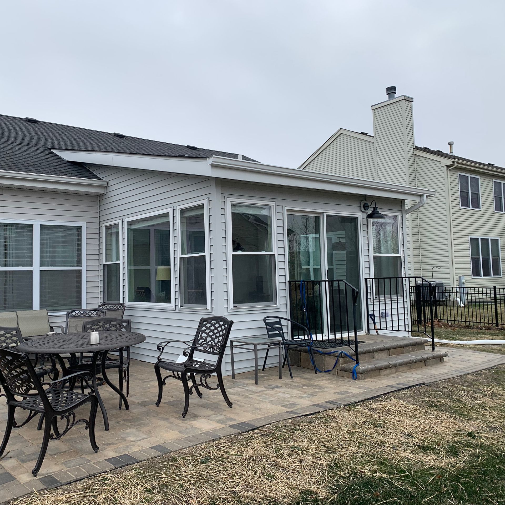 Patio with wrought iron furniture outside a white sunroom, paved with brick, on a cloudy day.