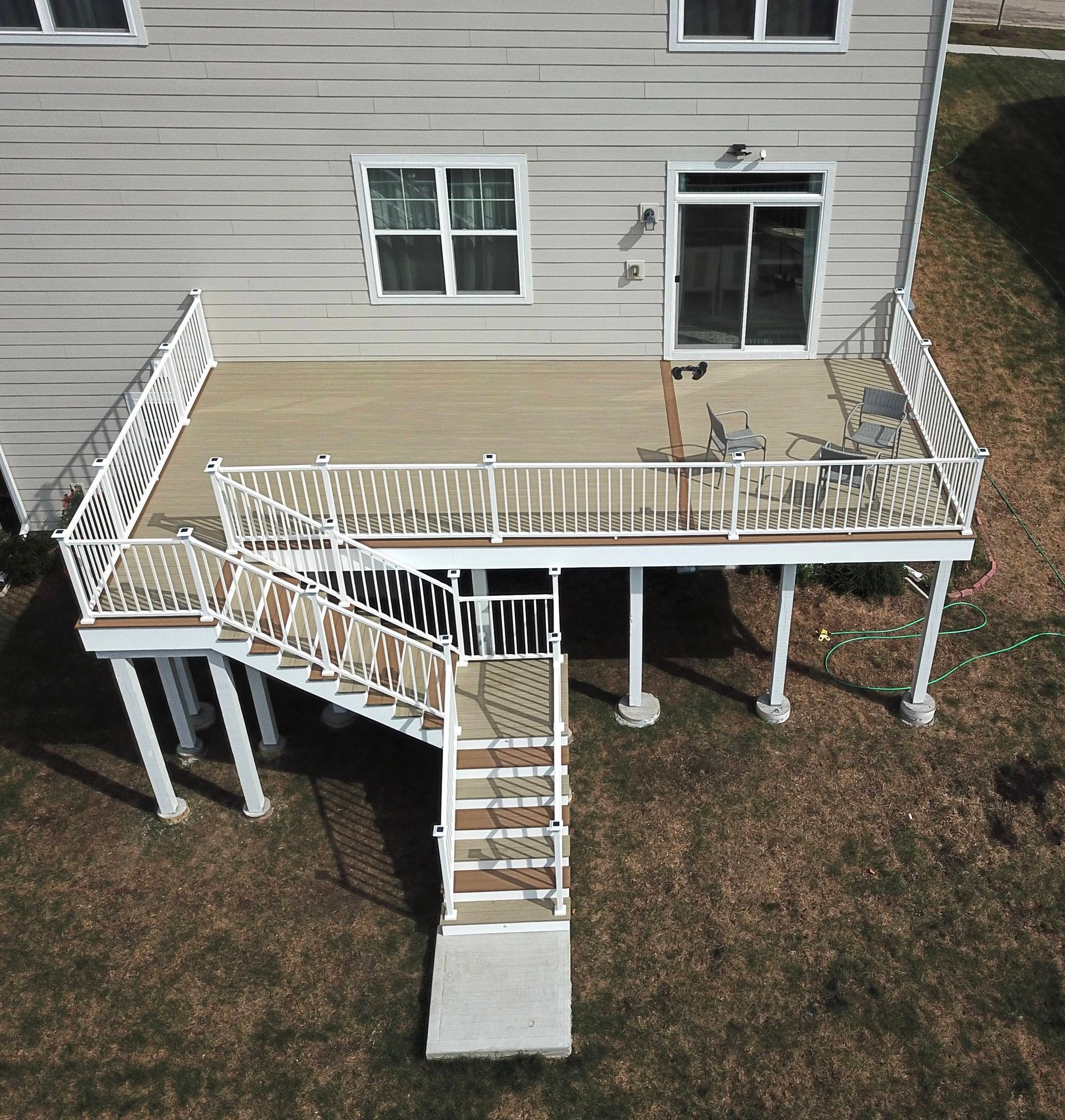 Elevated wooden deck attached to a house with stairs leading to a concrete base. White railings and supports.