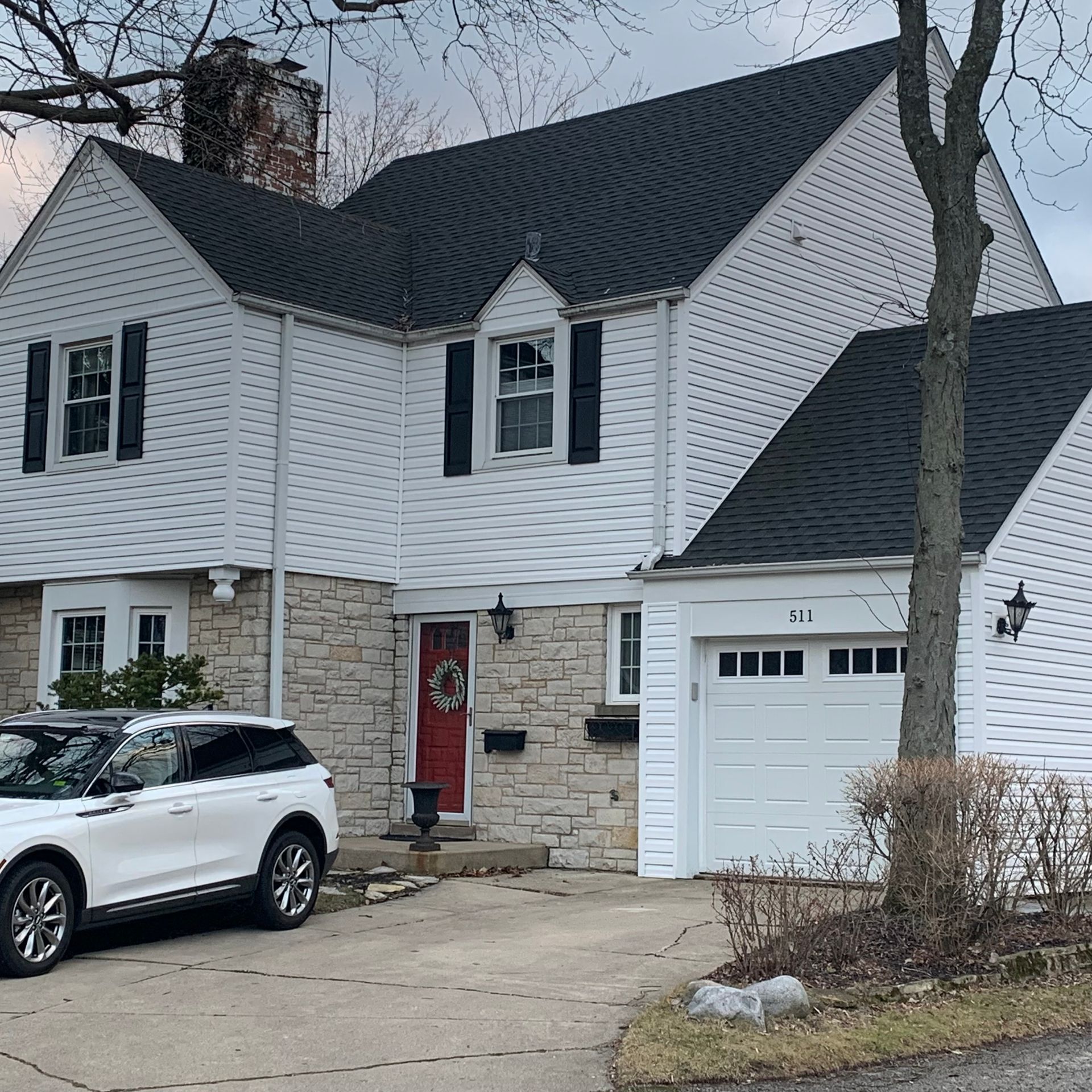 White house with black roof, shutters, and red door. White SUV parked in driveway.