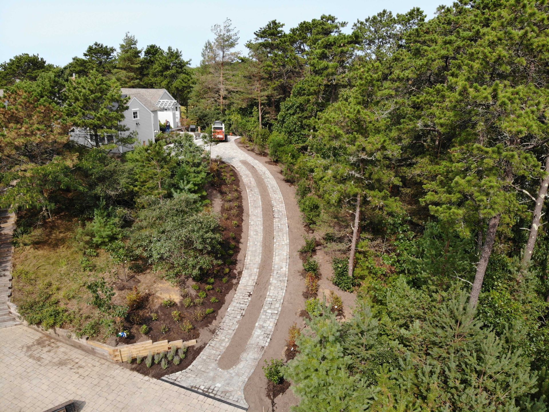 An aerial view of a stone-paved driveway winding through a lush green wooded landscape toward a house.