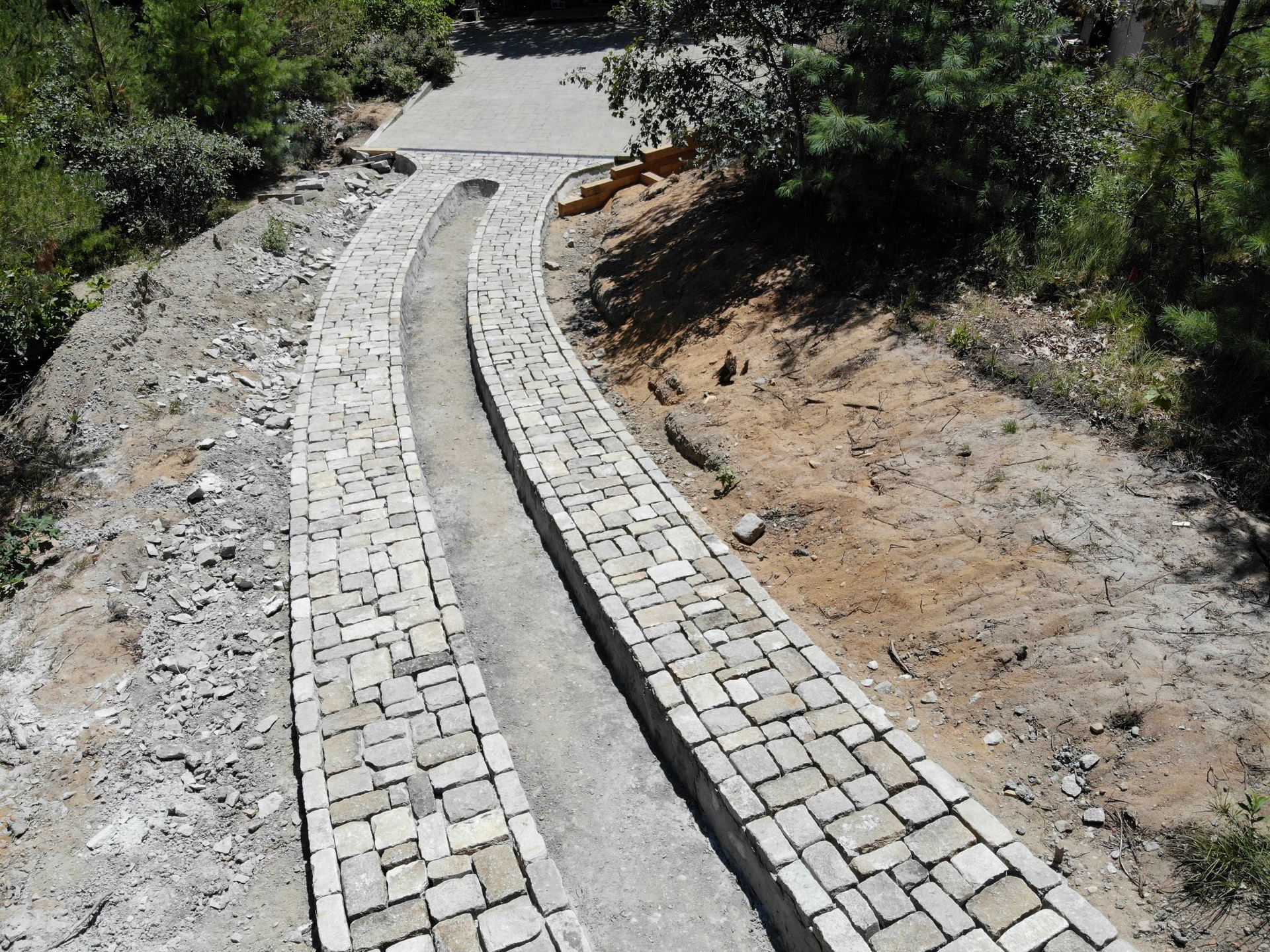A curved stone driveway with two parallel tracks of paved bricks set into a dirt hillside.