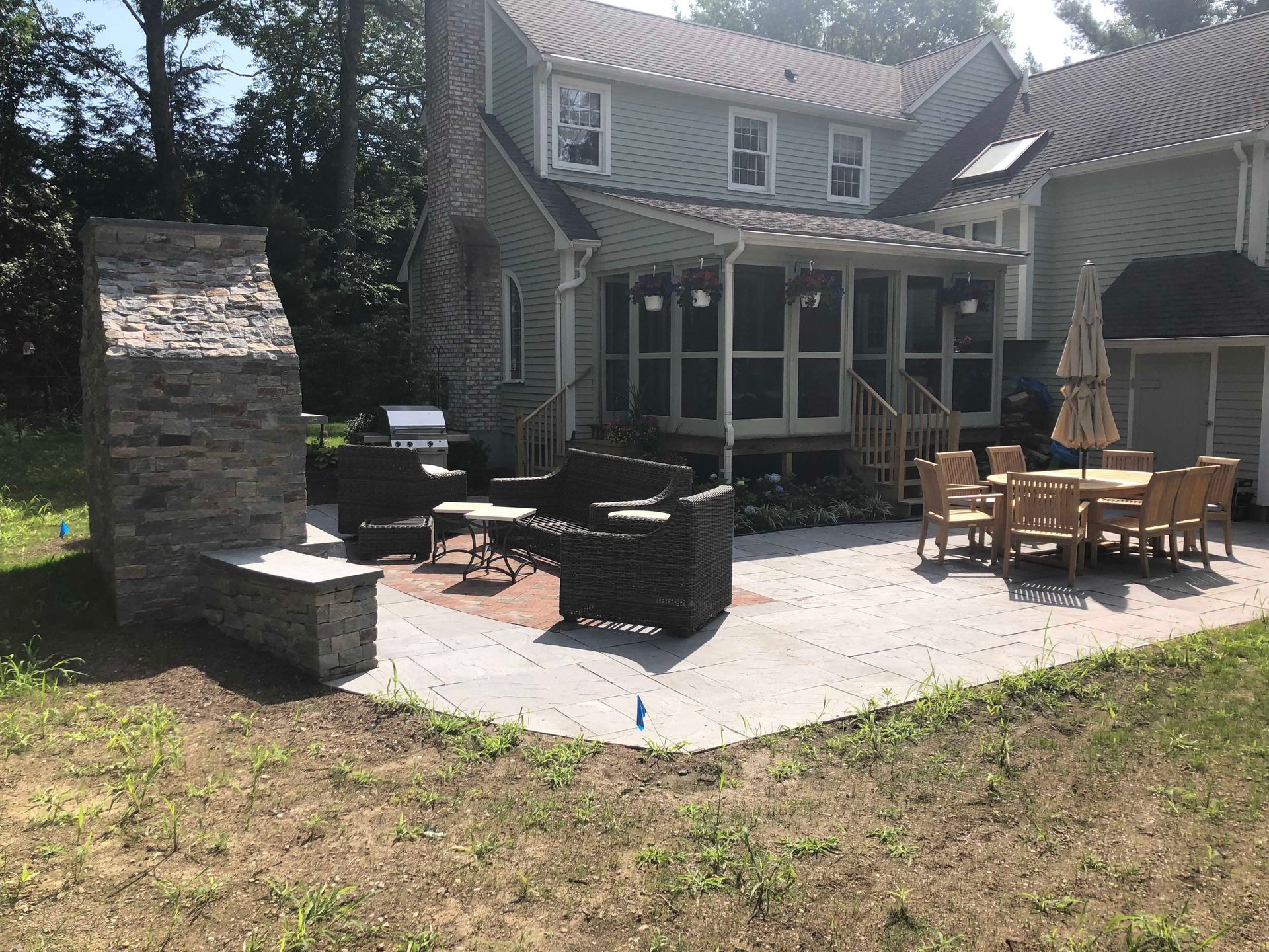 A stone outdoor fireplace and patio with lounge furniture and a dining set behind a house with a screened-in porch.