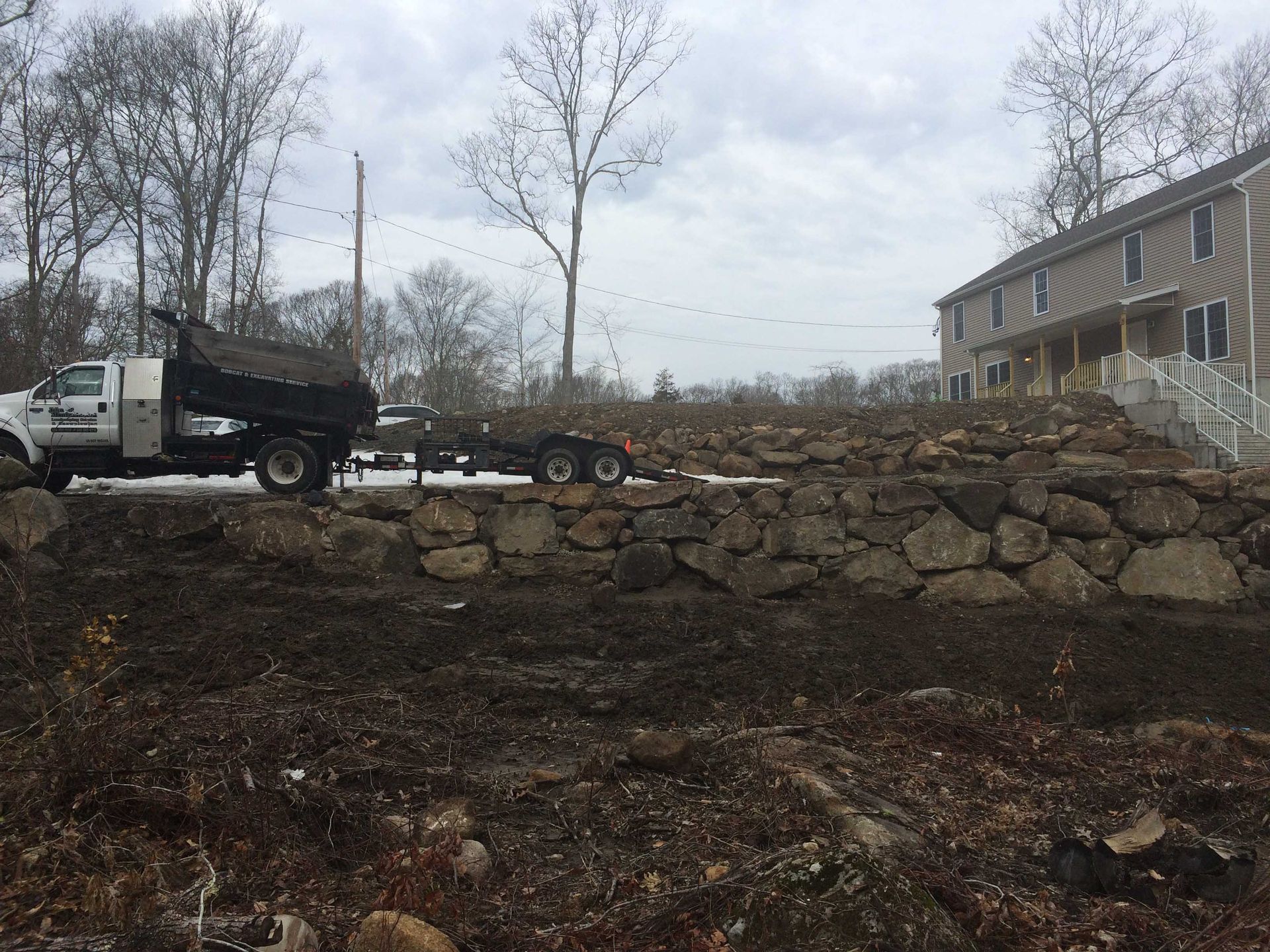 A white utility truck parked near a large, newly constructed boulder retaining wall in front of a residential building.