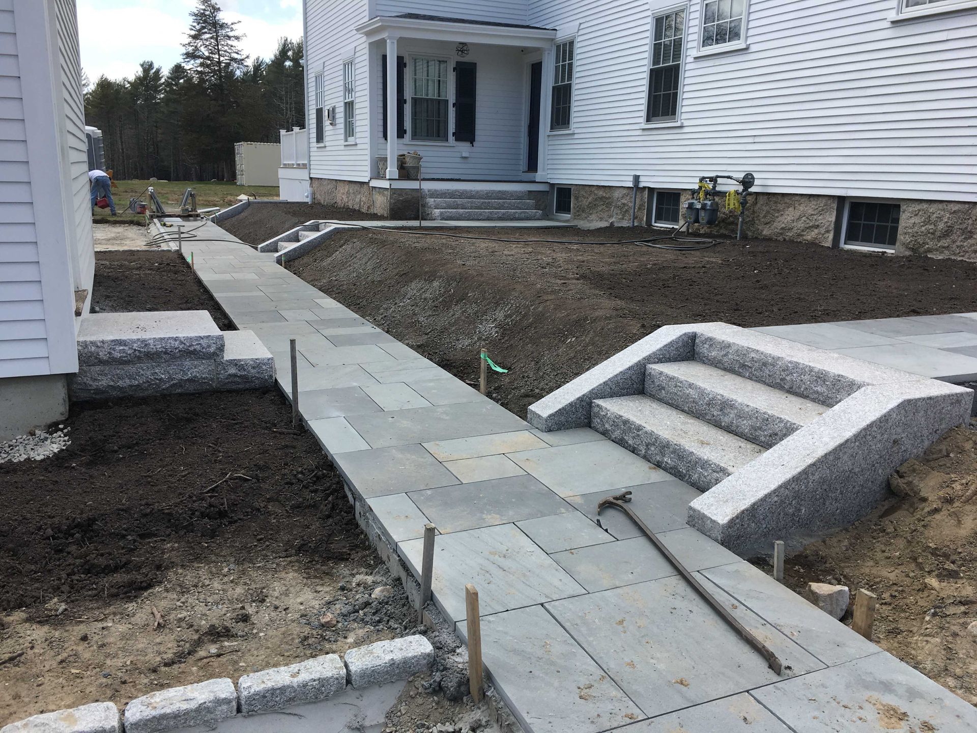 A stone walkway with granite steps and edging leads to the entrance of a white house surrounded by fresh landscaping.