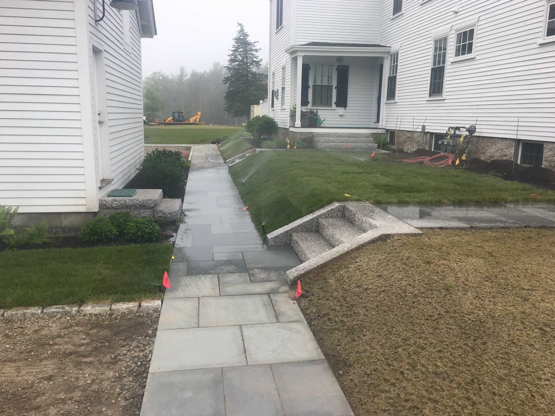 A stone walkway leads between two white houses toward a grassy yard with small concrete steps.
