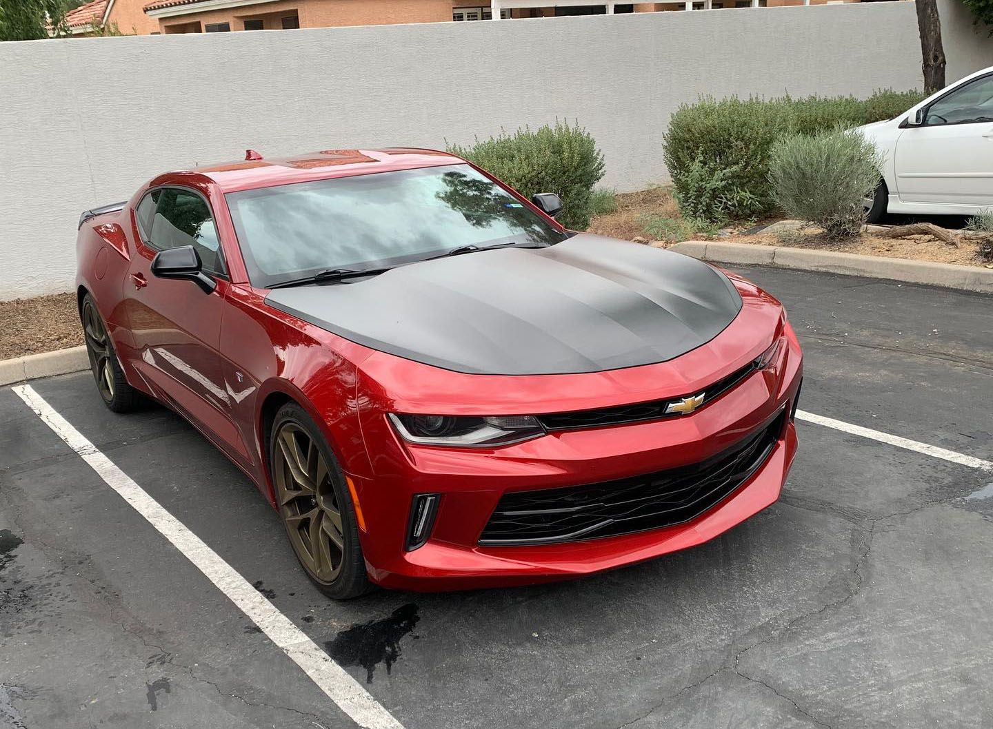 A red car with a black hood is parked in a parking lot.