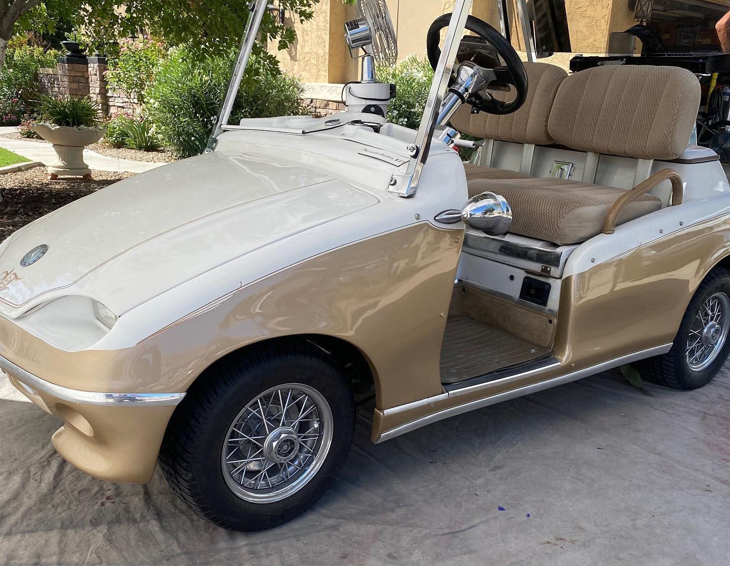 A gold and white golf cart is parked in a driveway.