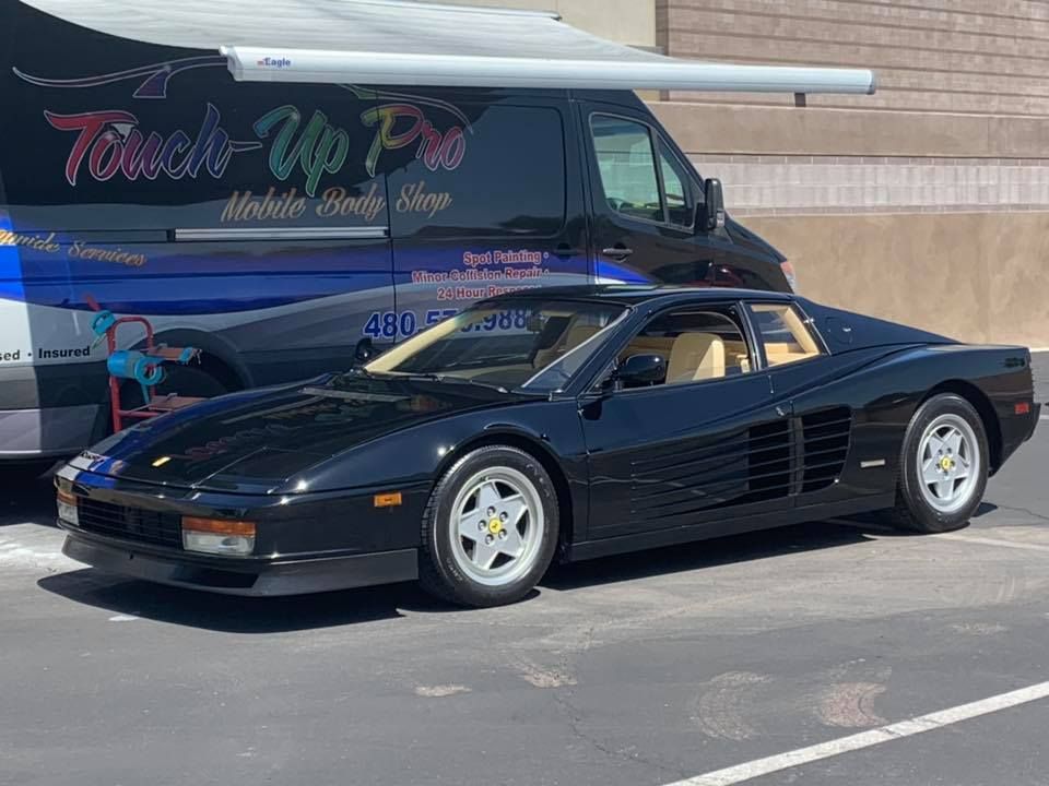 A black ferrari is parked in a parking lot next to a van.