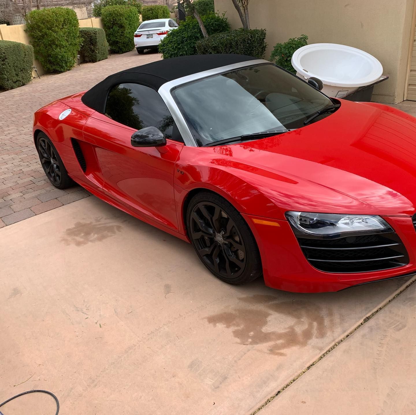 A red sports car with a black top is parked in a driveway.