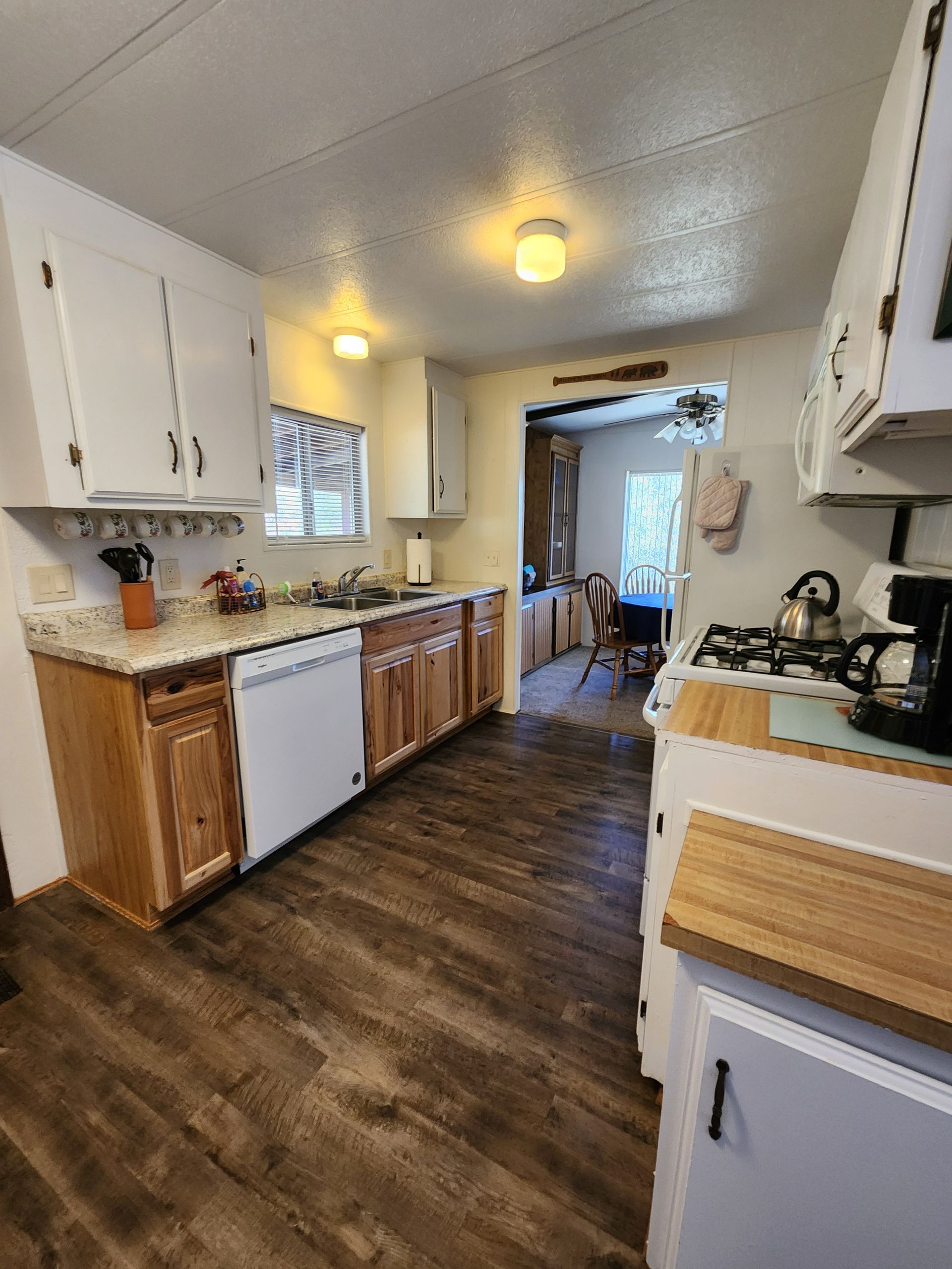A kitchen with wooden floors, white cabinets, a stove, a dishwasher, and a coffee maker.