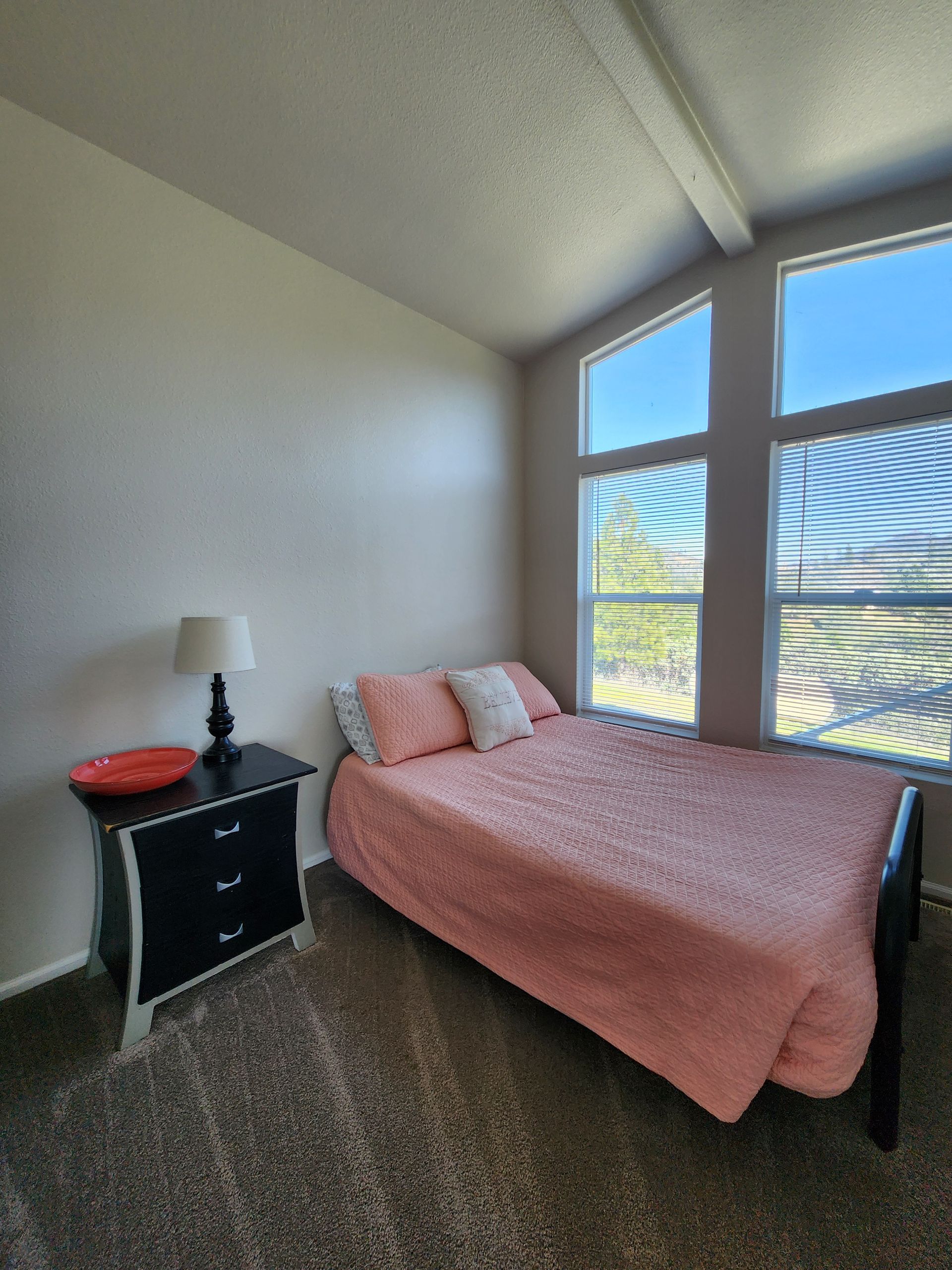 A bedroom with a bed , nightstand , lamp and windows