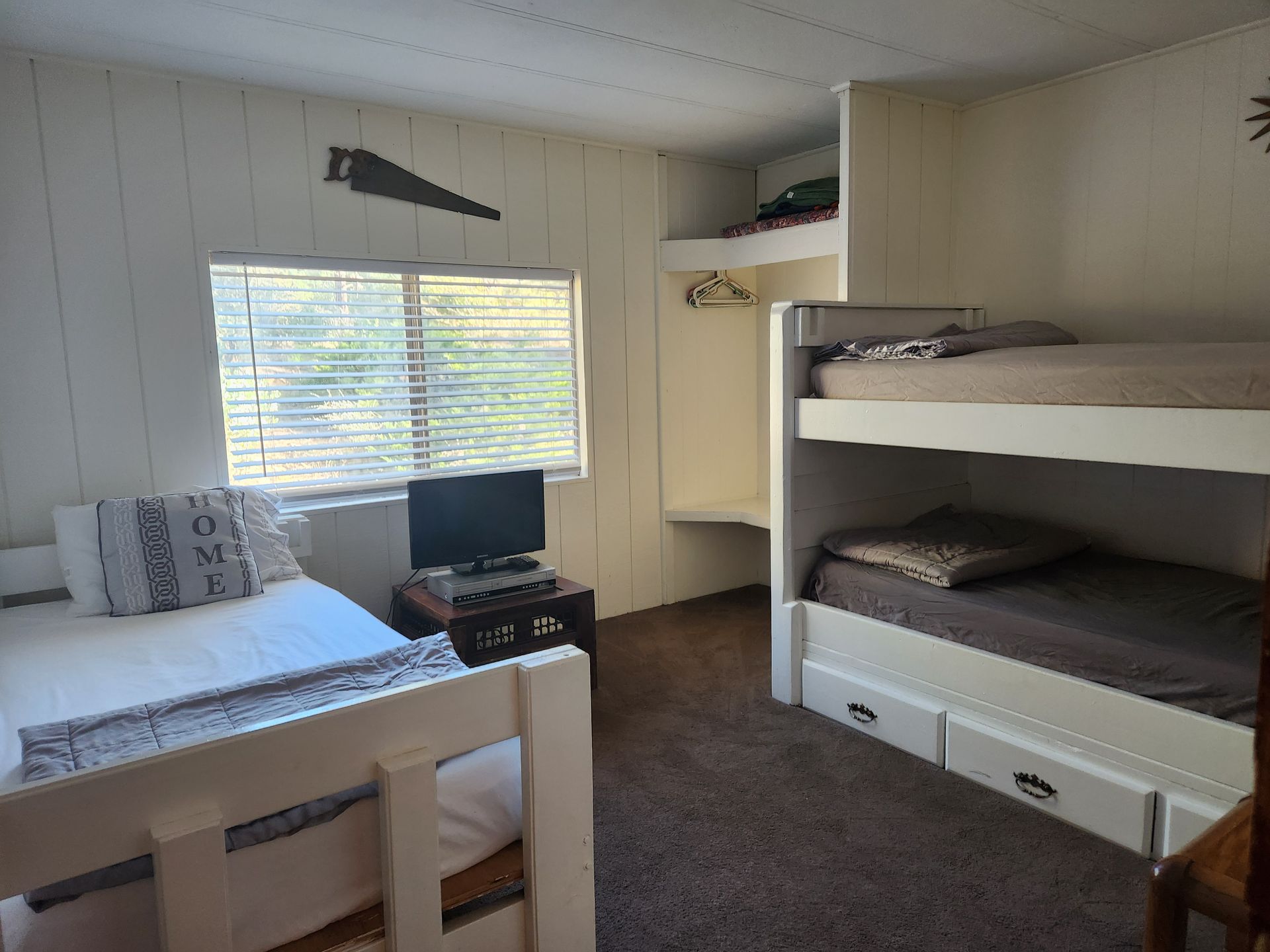 Bedroom with twin bed, bunk beds, window with blinds, and TV. Neutral colors.