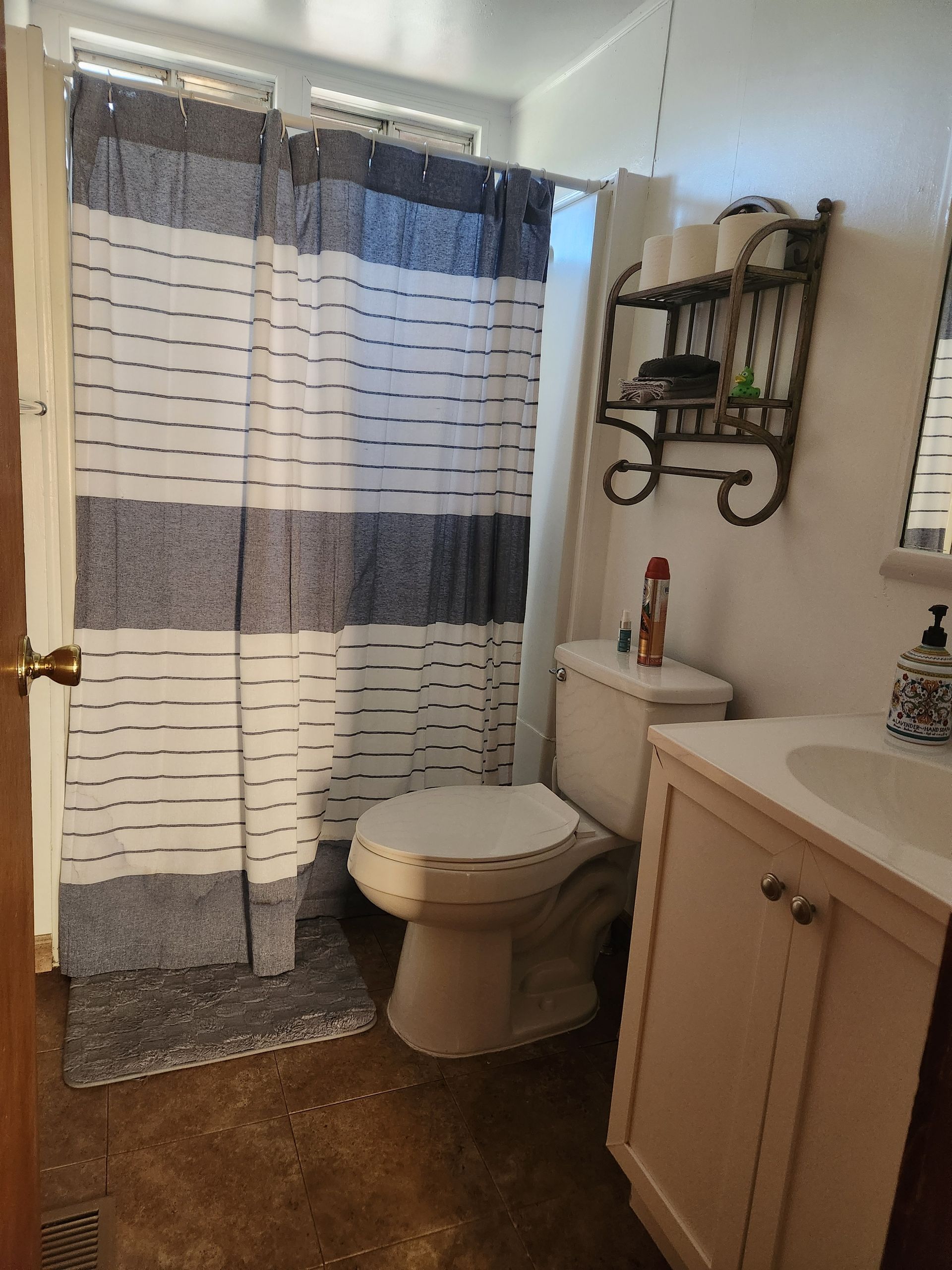 Bathroom with striped shower curtain, toilet, sink, and shelves.