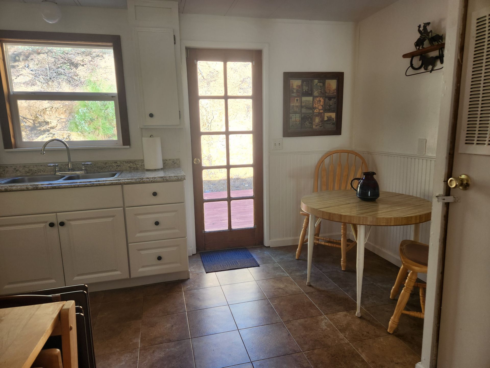 Small kitchen with a sink, white cabinets, round table, door, and a window.