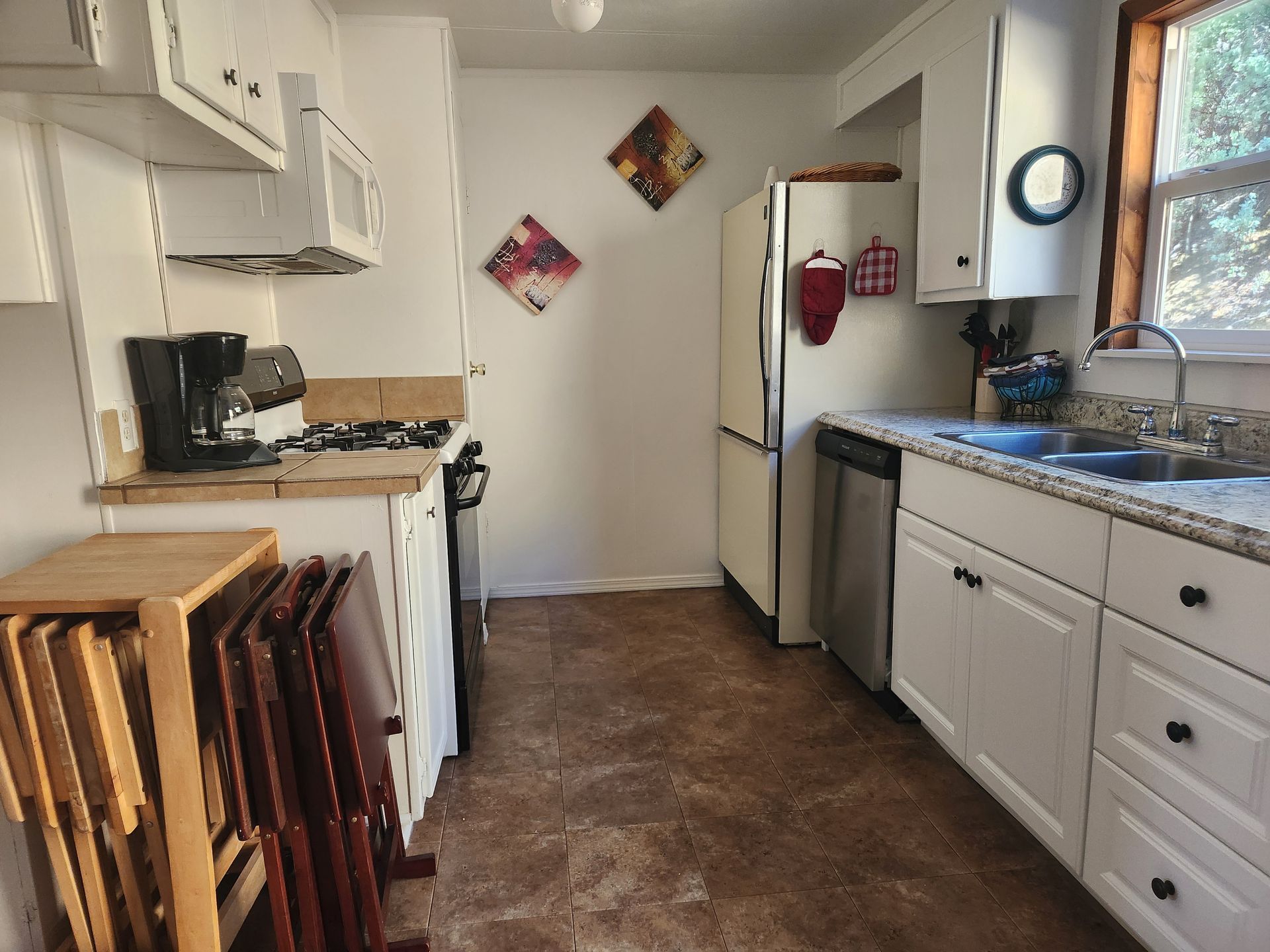 Small kitchen with white cabinets, appliances, and brown flooring. A table is folded up near the oven.