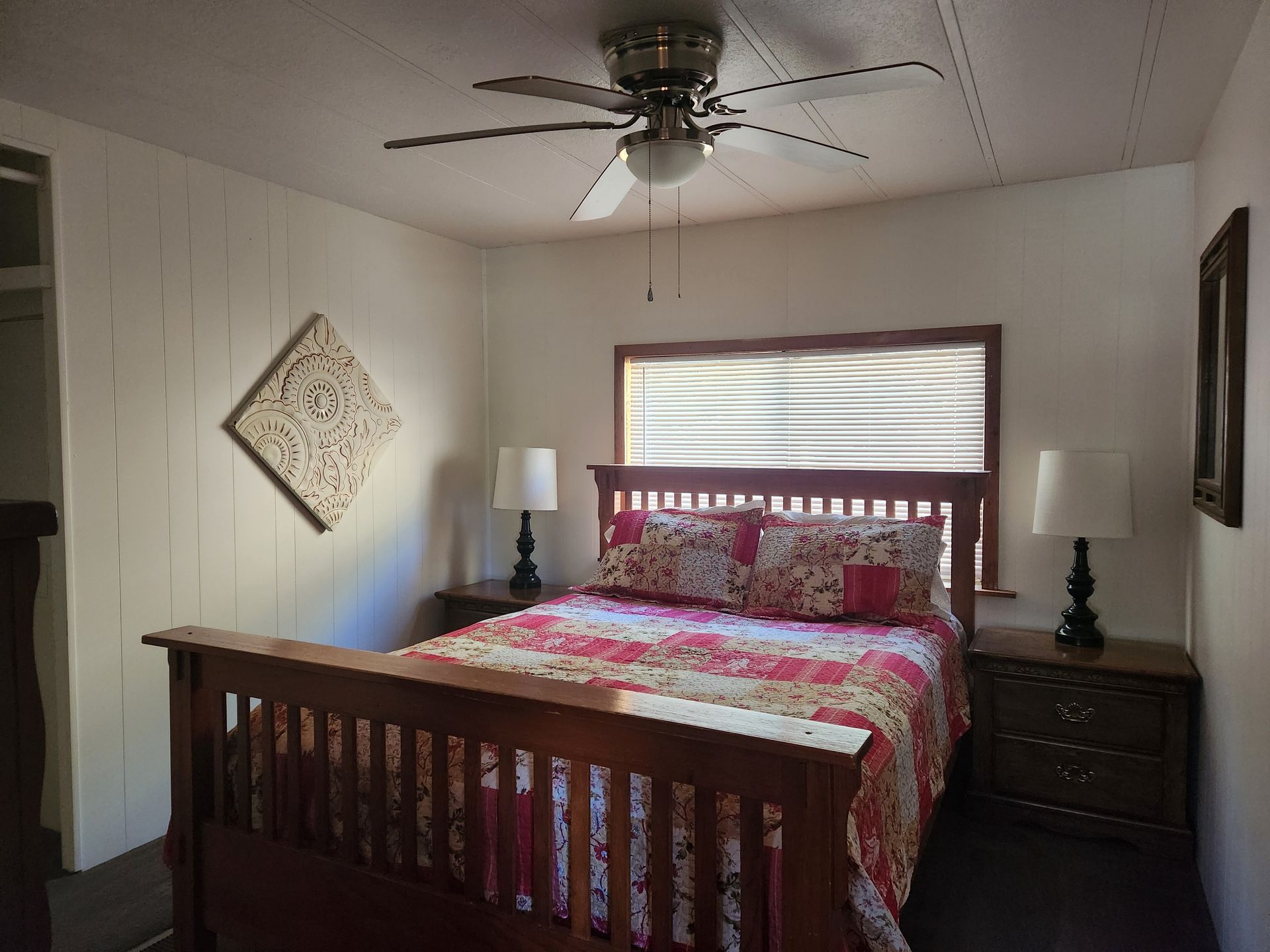 Bedroom with wooden bed, nightstands, decorative quilt, and ceiling fan.