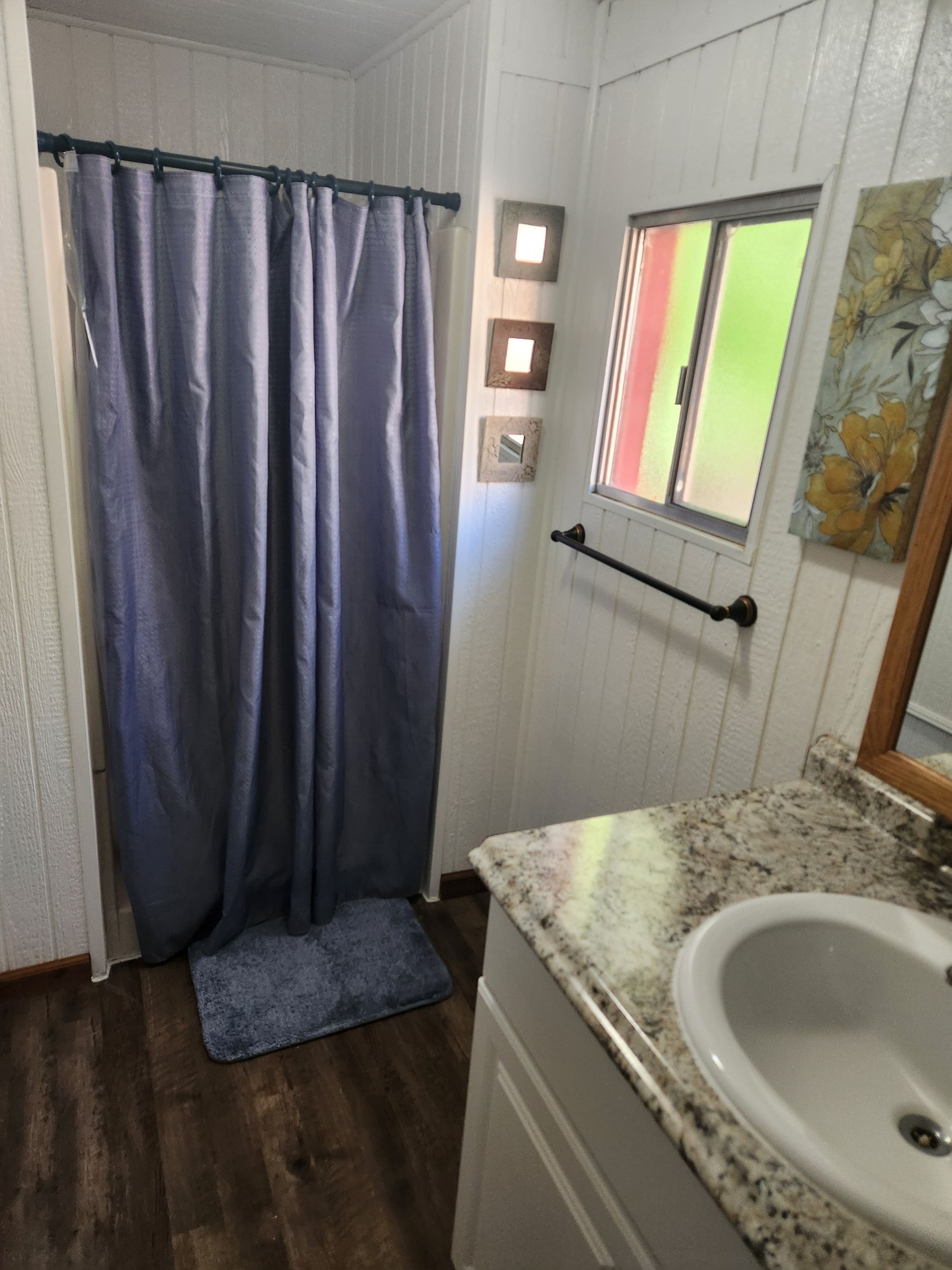Bathroom with a blue shower curtain, sink, and window with a view.