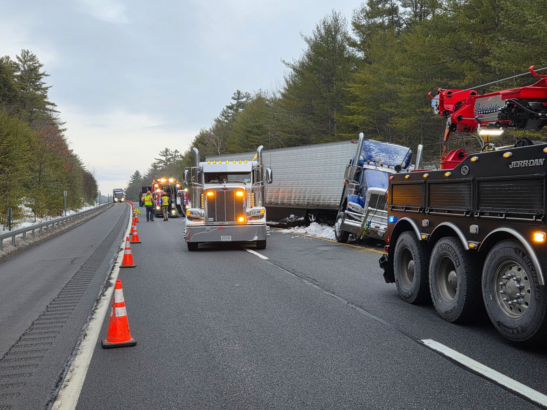 Highway accident scene with emergency vehicles, orange cones, and a damaged semi-truck blocking lanes