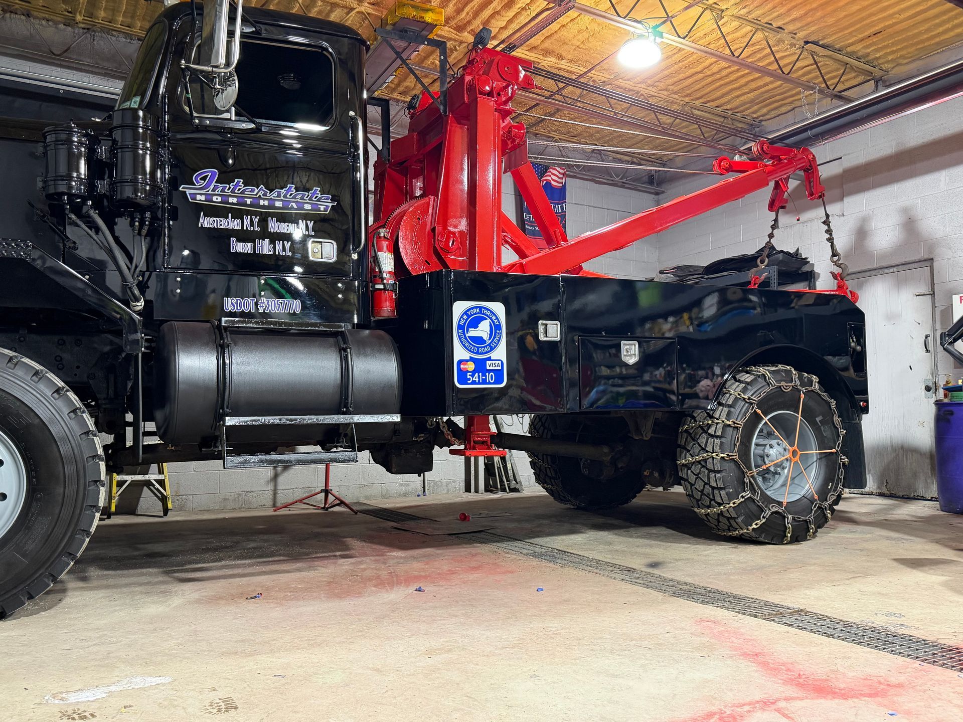 Black tow truck in a garage with a red crane arm and large rear wheel