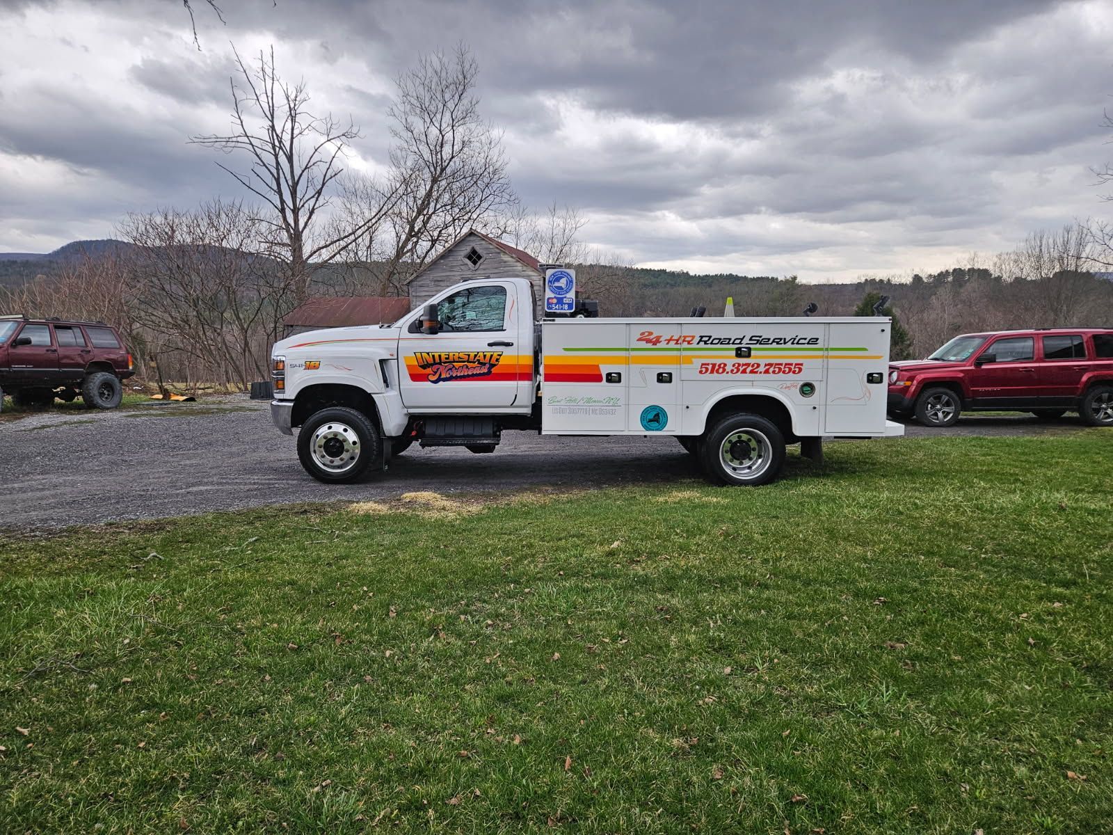 White utility truck with orange signage parked on grass under a cloudy sky