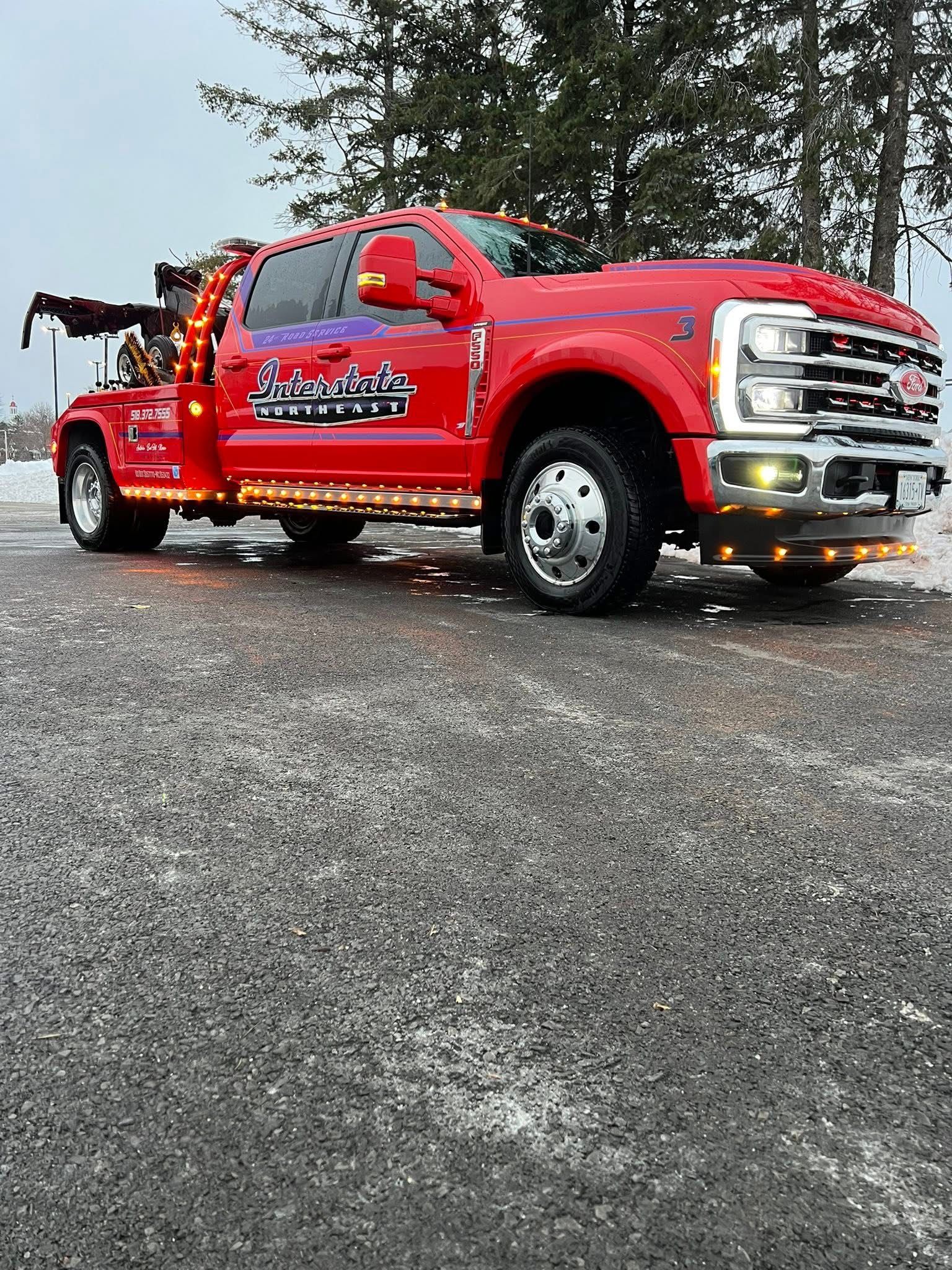 Red tow truck with lights on, parked on wet pavement near trees.