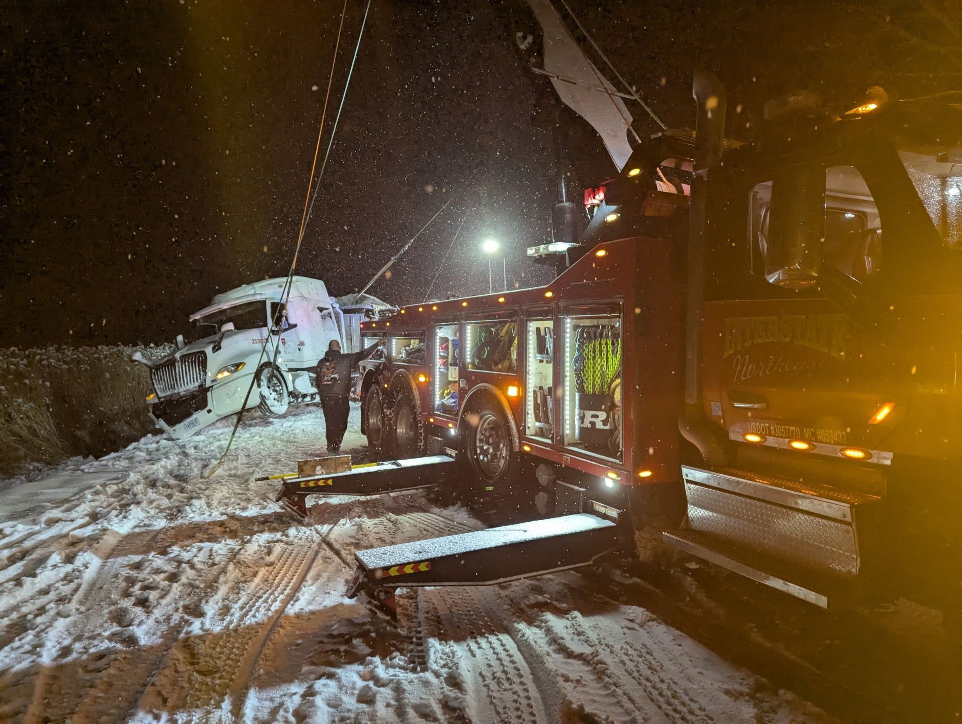 Snowy nighttime roadside crash with firefighters and a wrecked car beside a fire truck