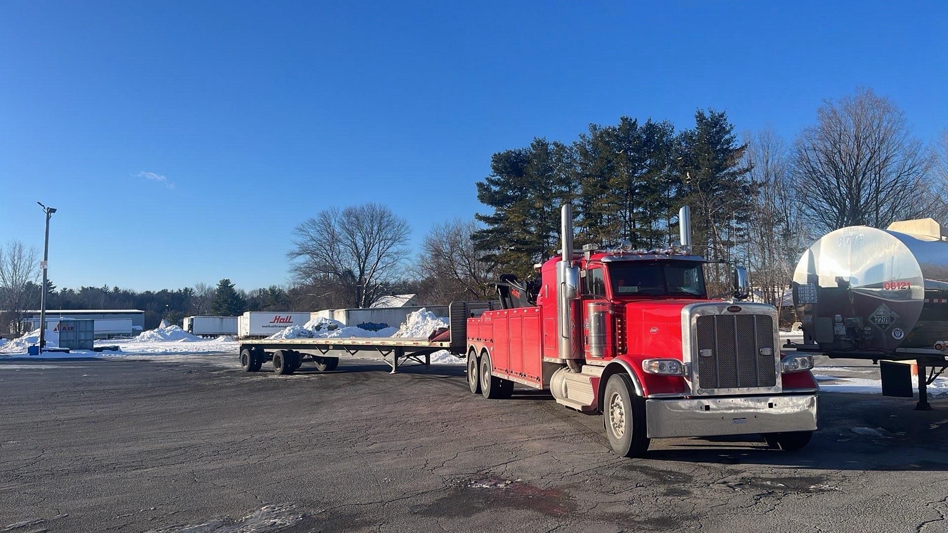 Red semi truck parked on a gravel lot beside a white tanker trailer under a clear blue sky.