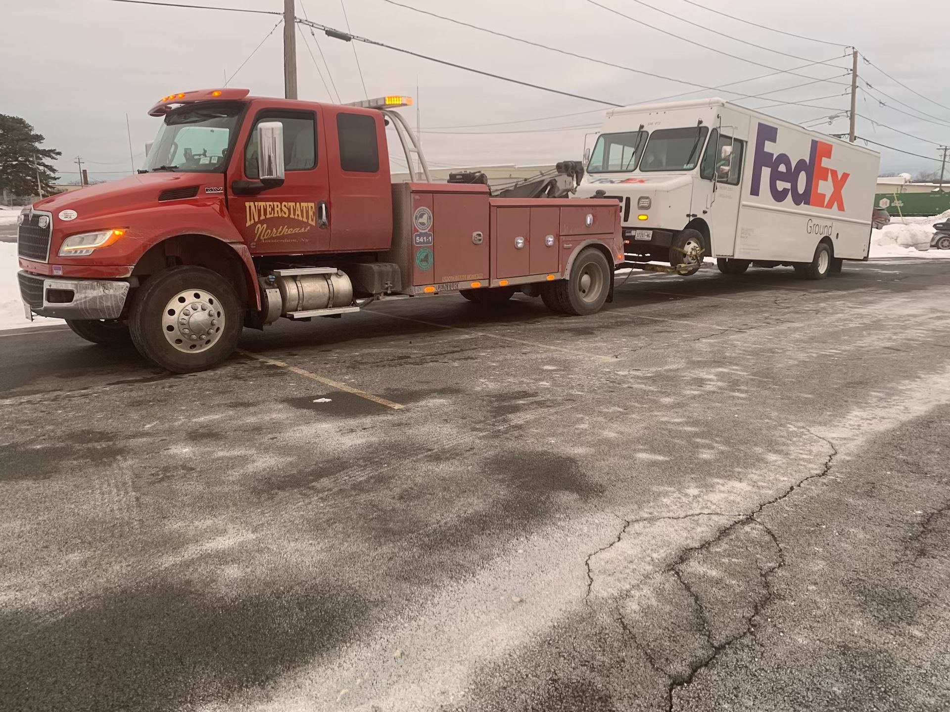 Red tow truck hauling a FedEx delivery van on a snowy roadside