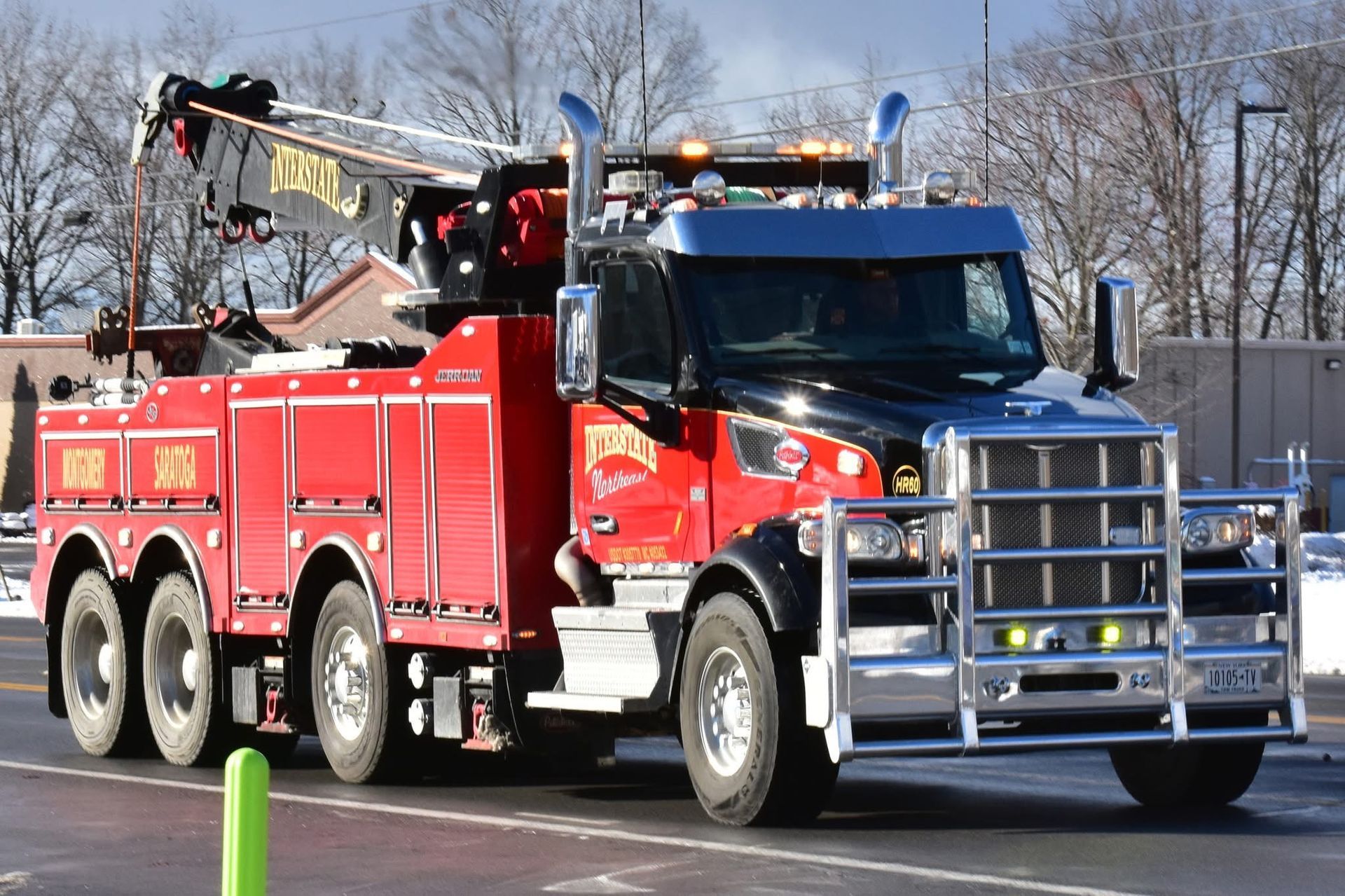 Red fire truck with ladder driving on a road, trees and a fence in the background.